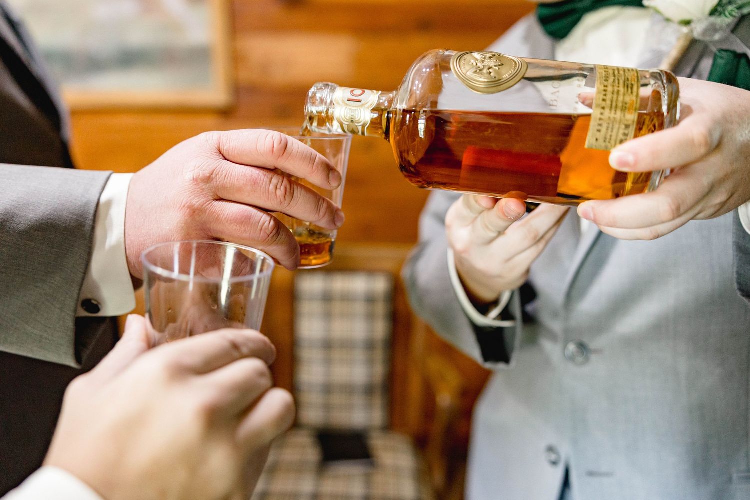 Groomsmen pouring whiskey from a crystal decanter into glasses during wedding day preparations.