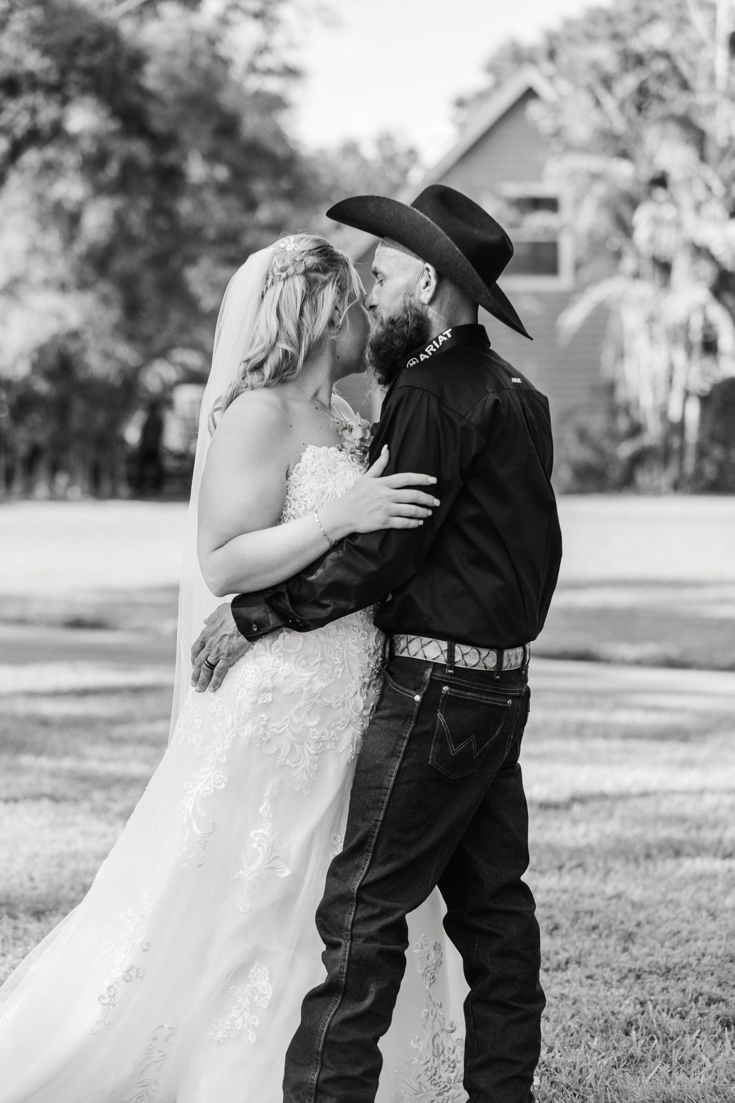 Black and white photo of bride and groom sharing a kiss outdoors in a grassy setting.