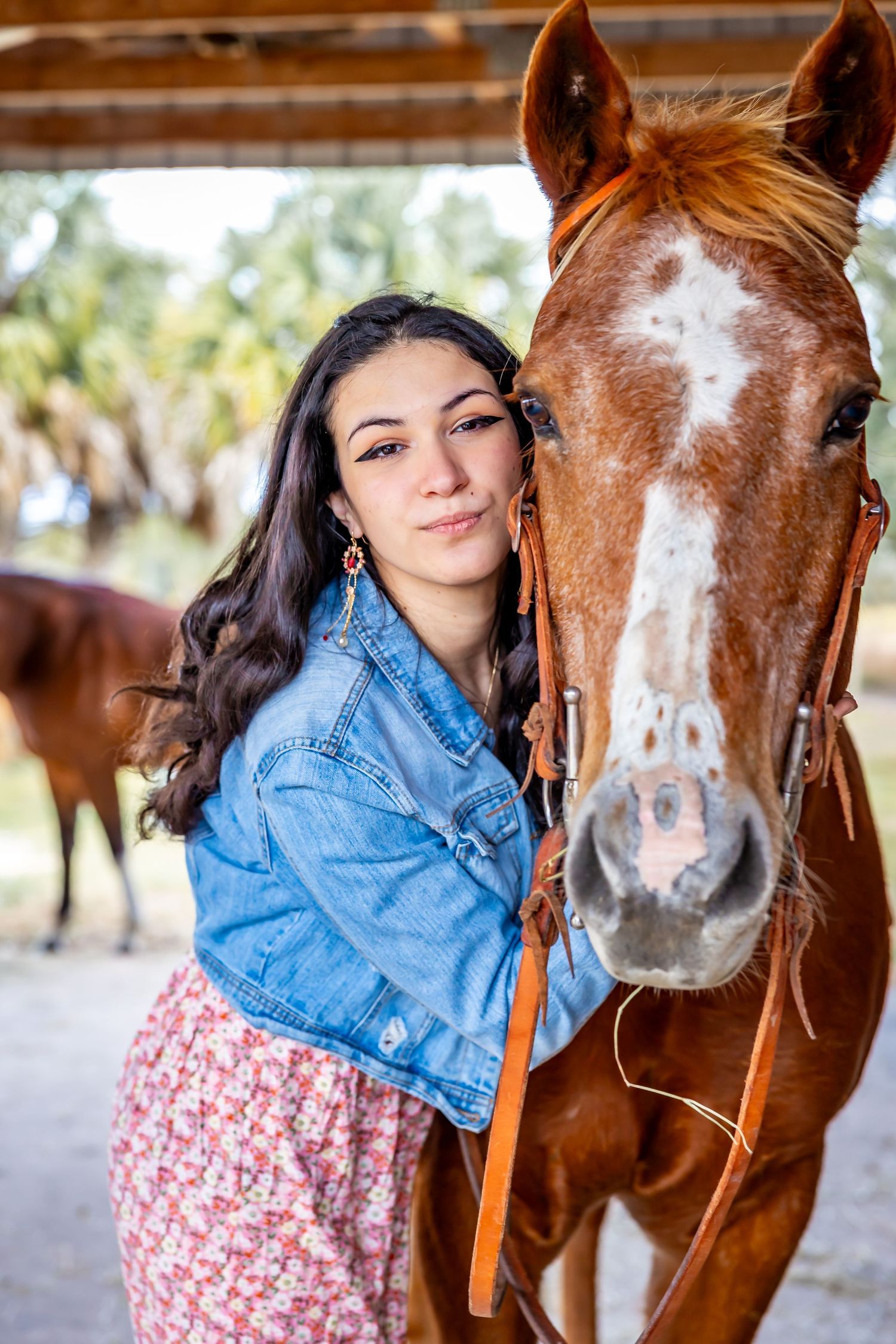 Young woman in denim jacket leaning affectionately against chestnut horse in stable.