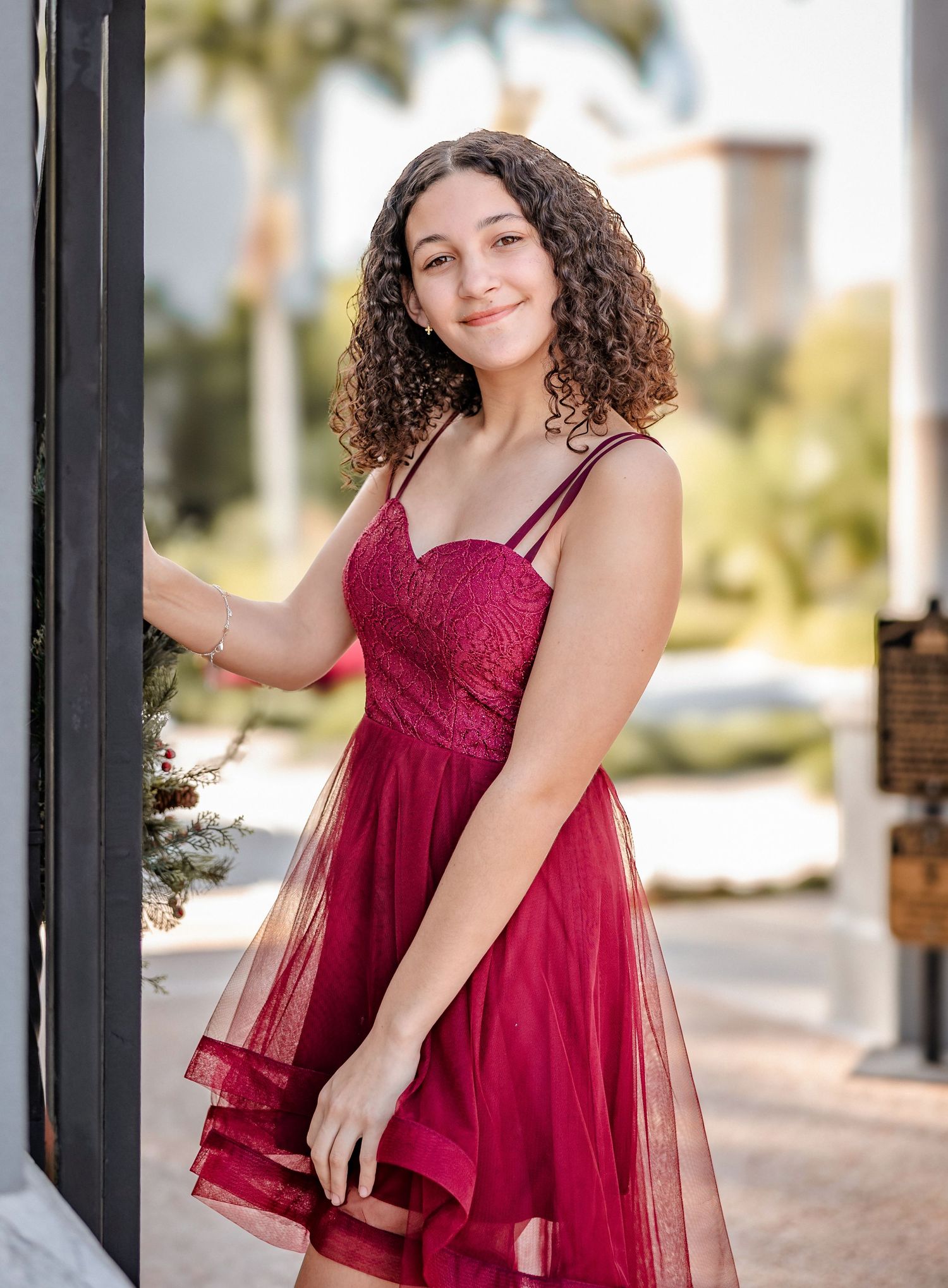 Young woman in a red tulle lace dress smiling outdoors during a senior portrait session.