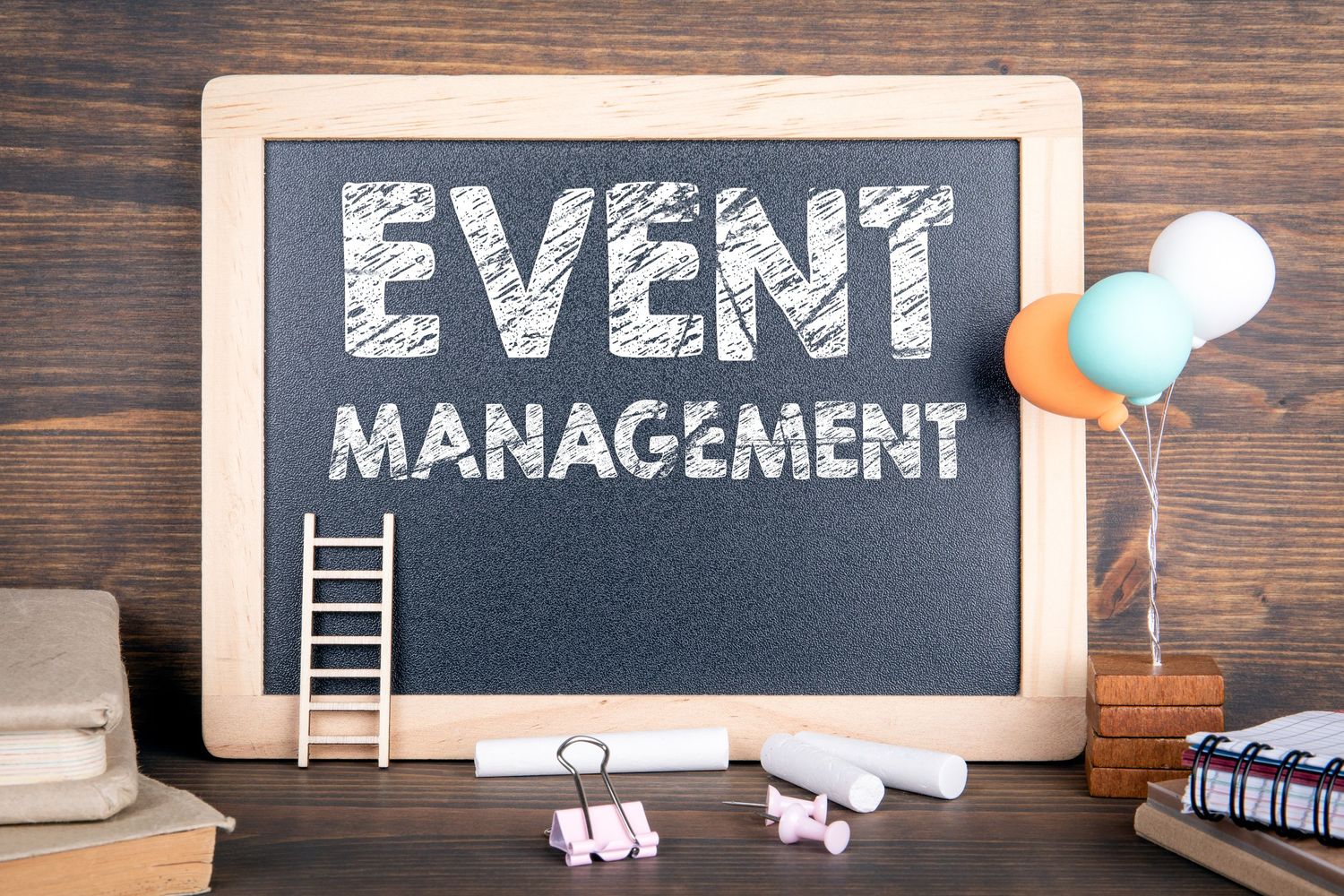 Chalkboard sign reading Event Management with balloons and decorative items on wooden background.