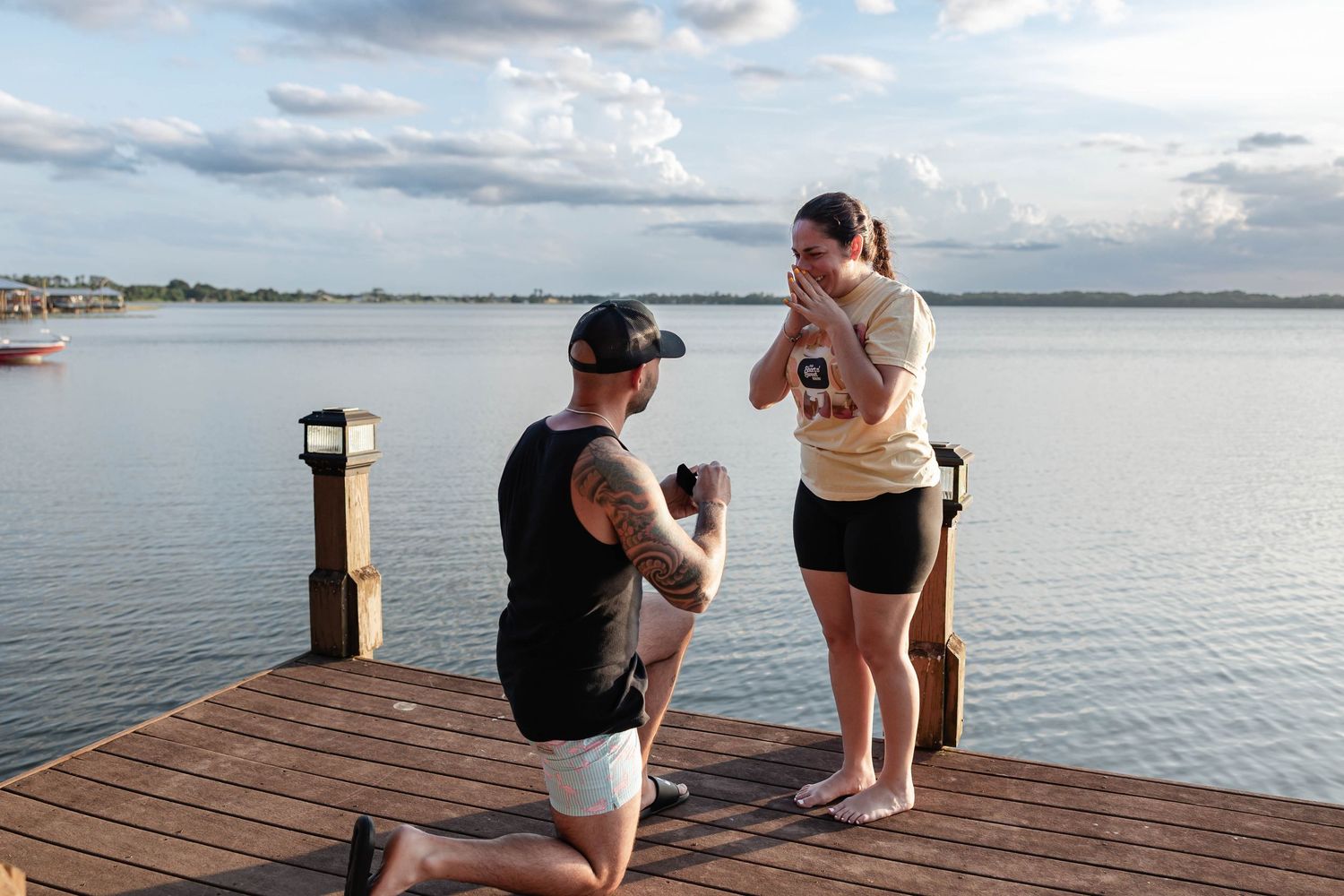 Man proposes to woman on wooden dock by lake at sunset, romantic marriage proposal scene.
