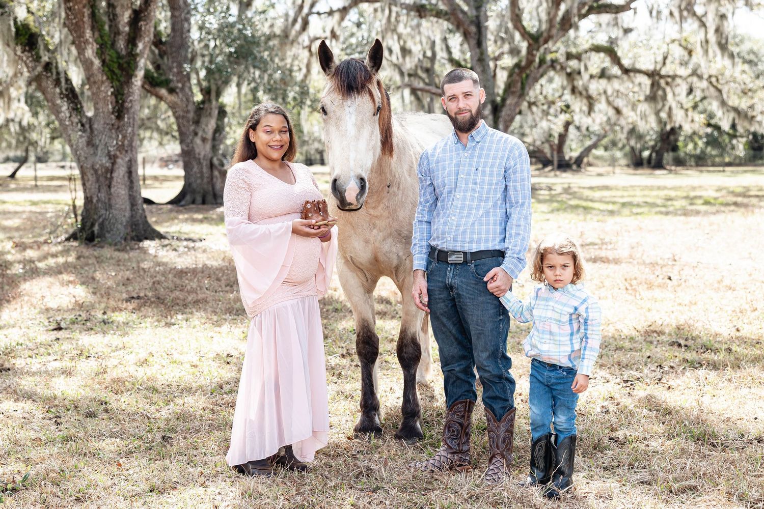 Maternity family portrait with horse, pregnant mother in pink dress, father, and young child.