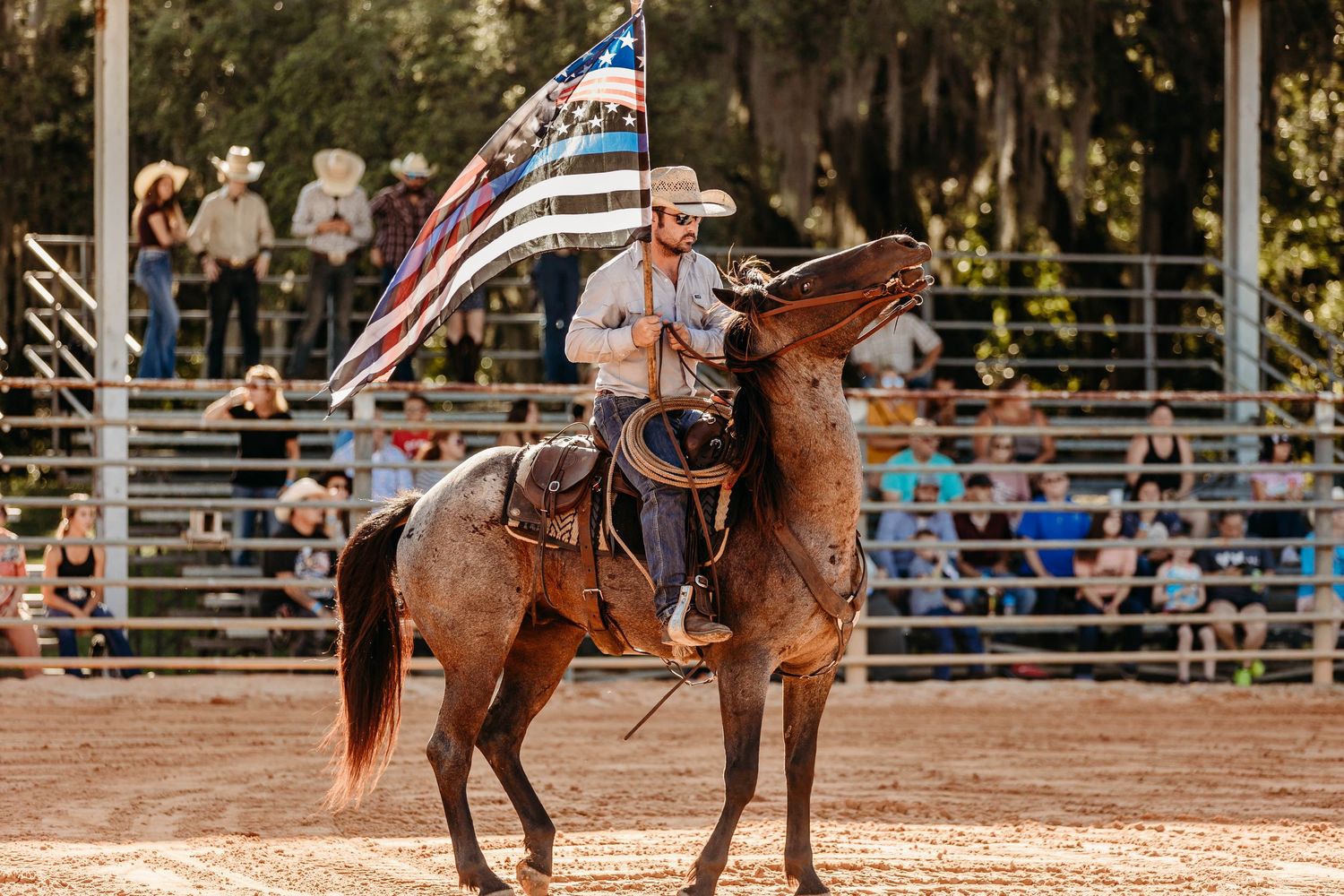 Cowboy on rearing horse carrying American flag during rodeo arena opening ceremony performance.