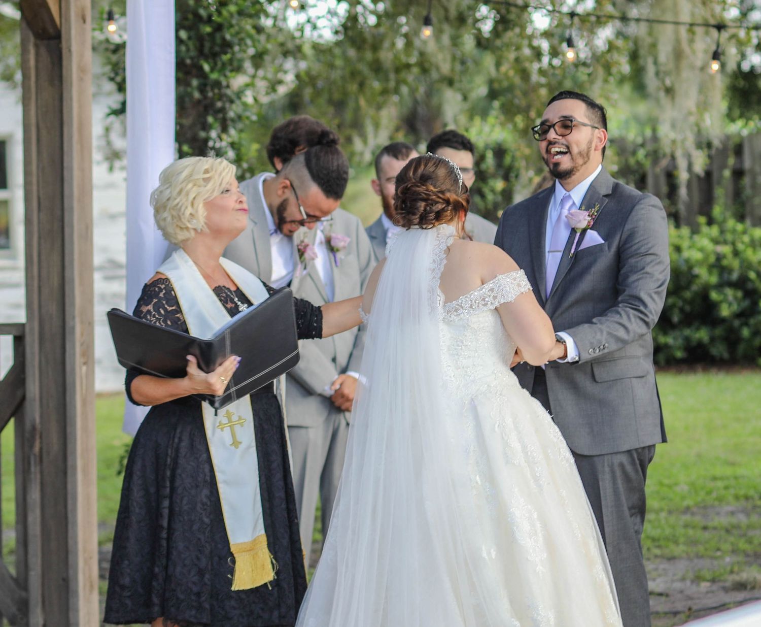 Joyful wedding party laughing and embracing after outdoor ceremony beneath Spanish moss-covered trees.