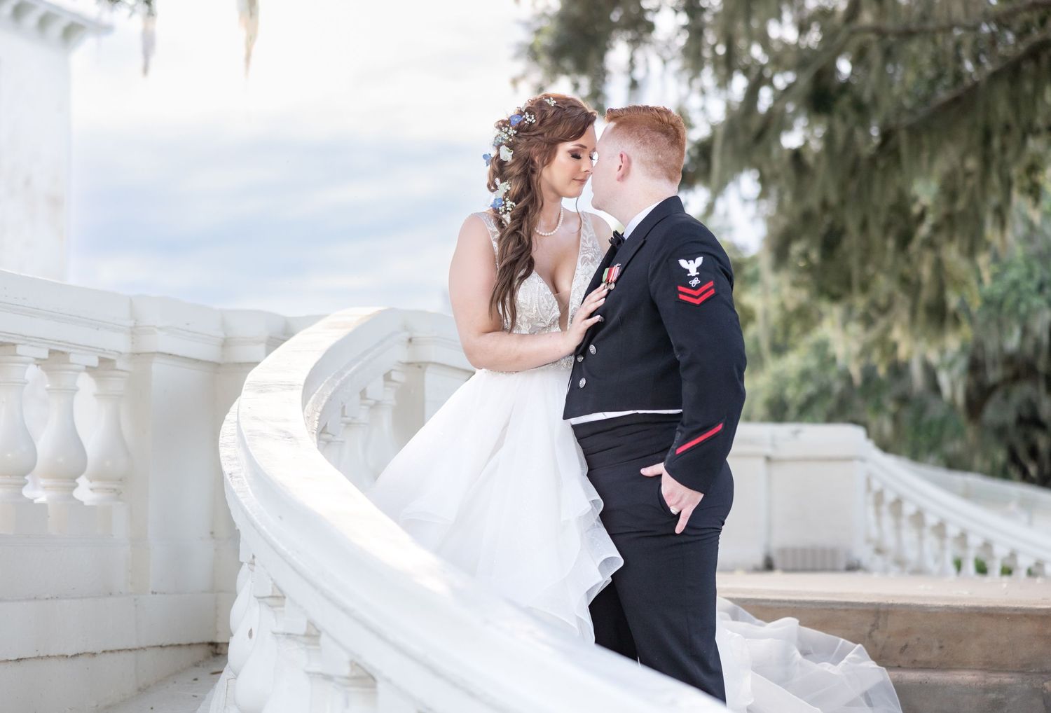A Navy groom in dress uniform shares a romantic moment with his bride on a white balcony.