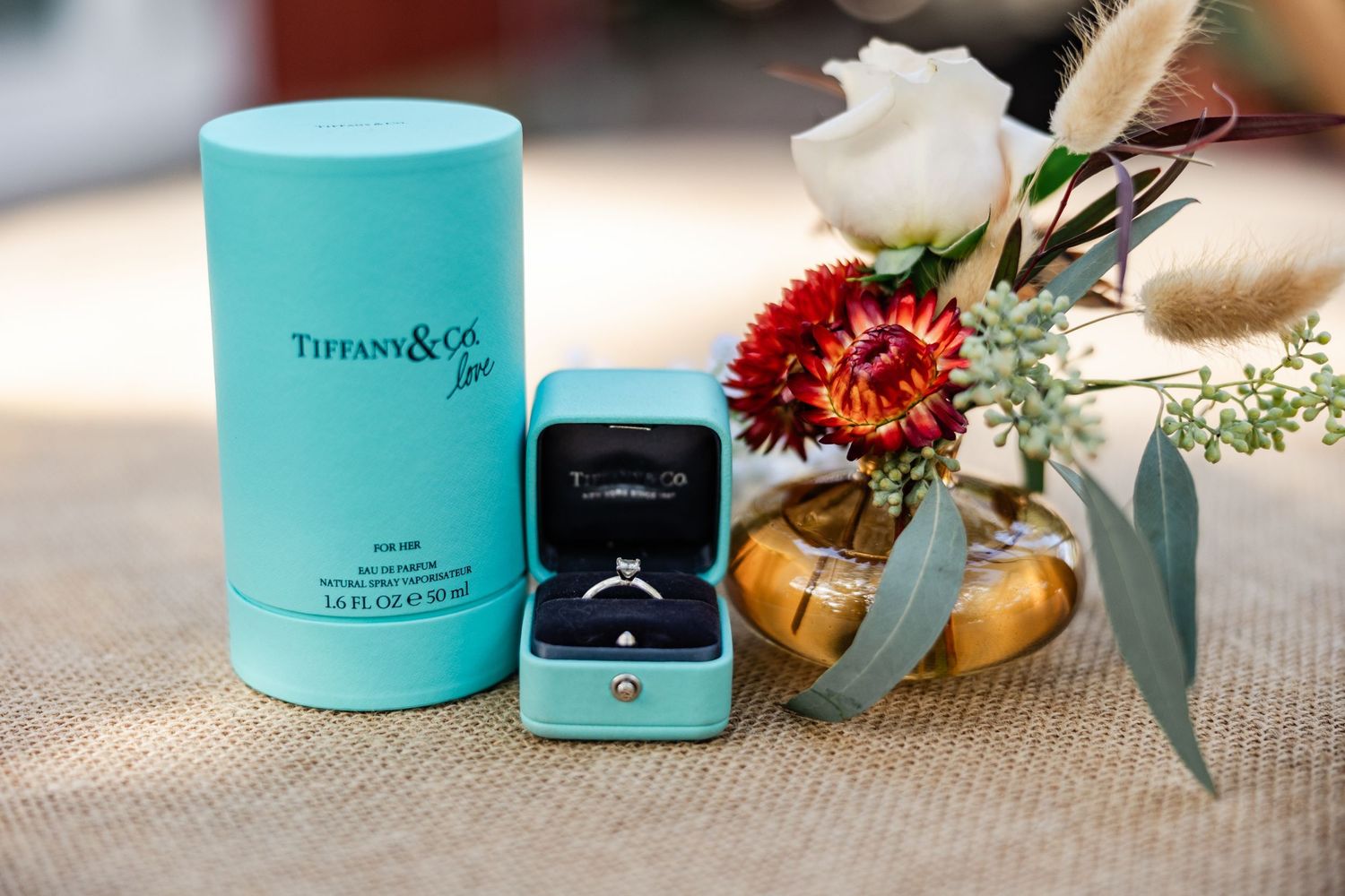 Tiffany and Co ring box with diamond engagement ring beside a floral arrangement.