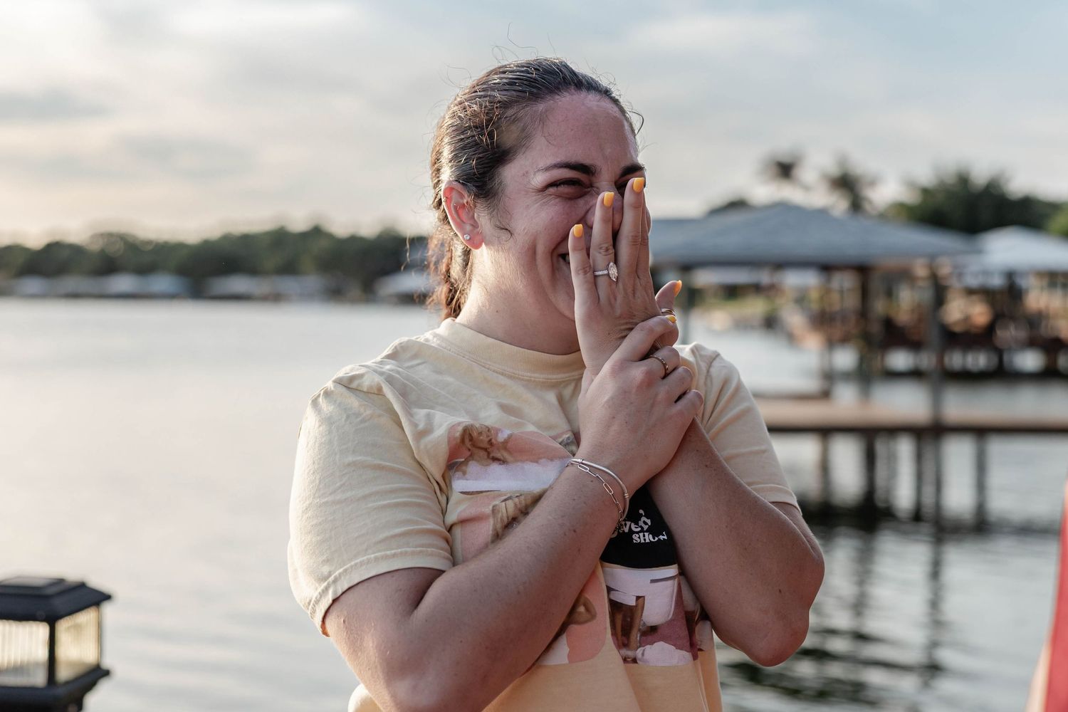 Emotional woman admiring her engagement ring by the waterfront at sunset.