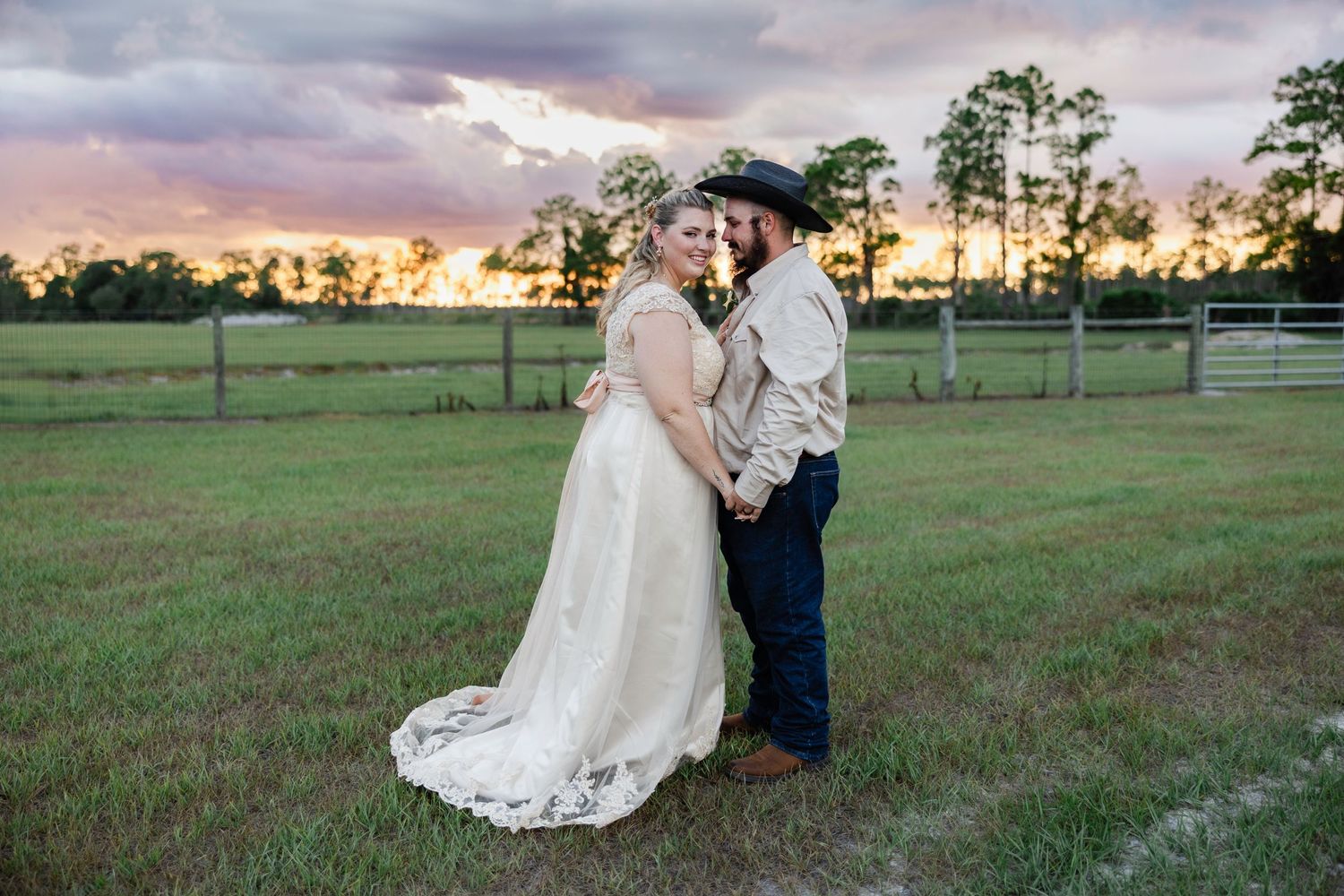 Bride and groom embrace romantically at golden sunset in open green field on their wedding day.