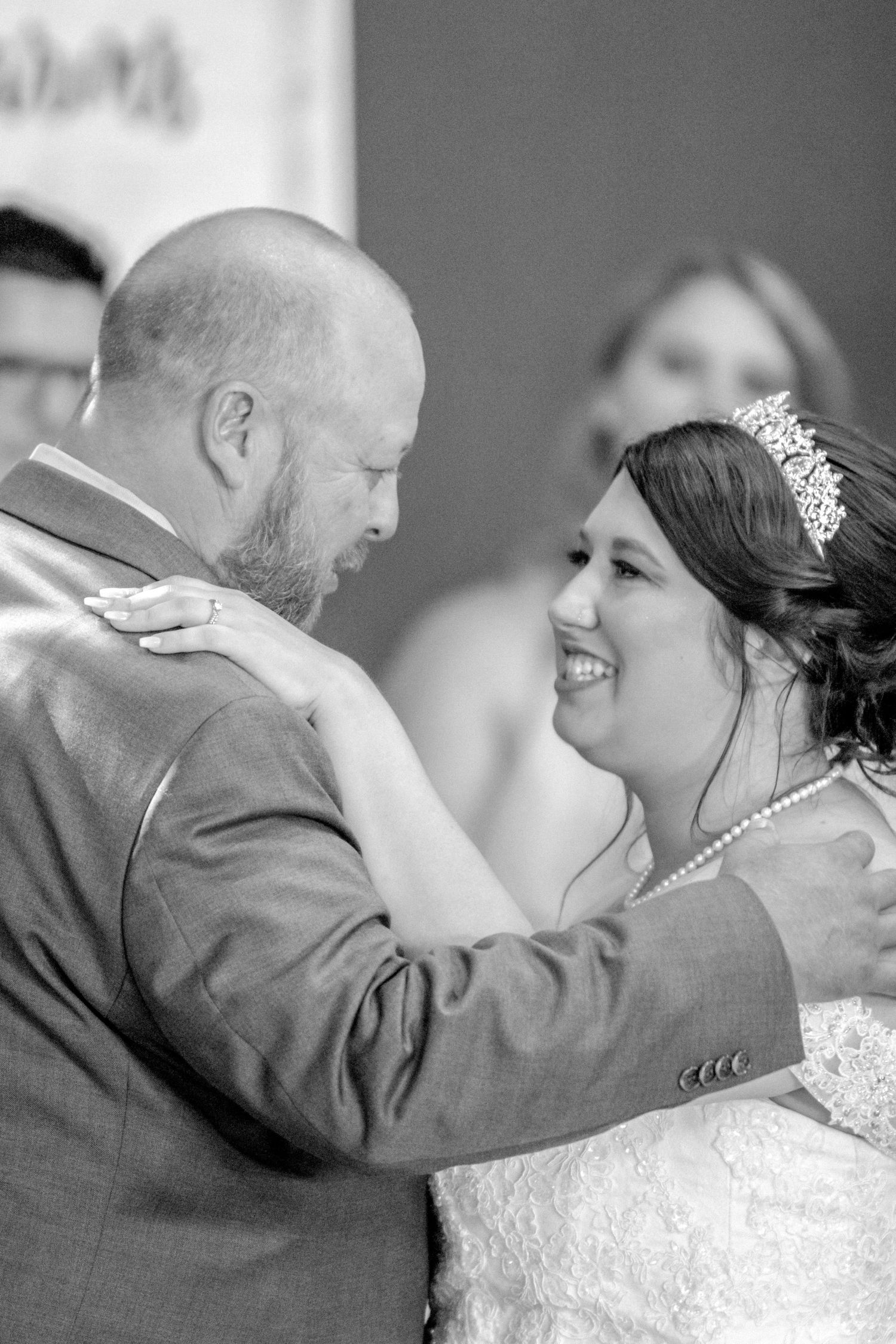 Black and white photo of bride and groom sharing first dance, bride smiling joyfully.