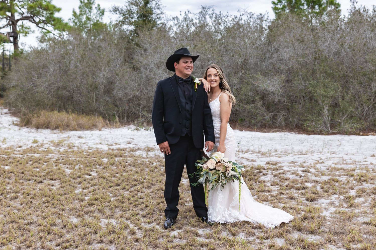 Bride and groom pose together in snowy outdoor setting, groom wearing black cowboy hat.