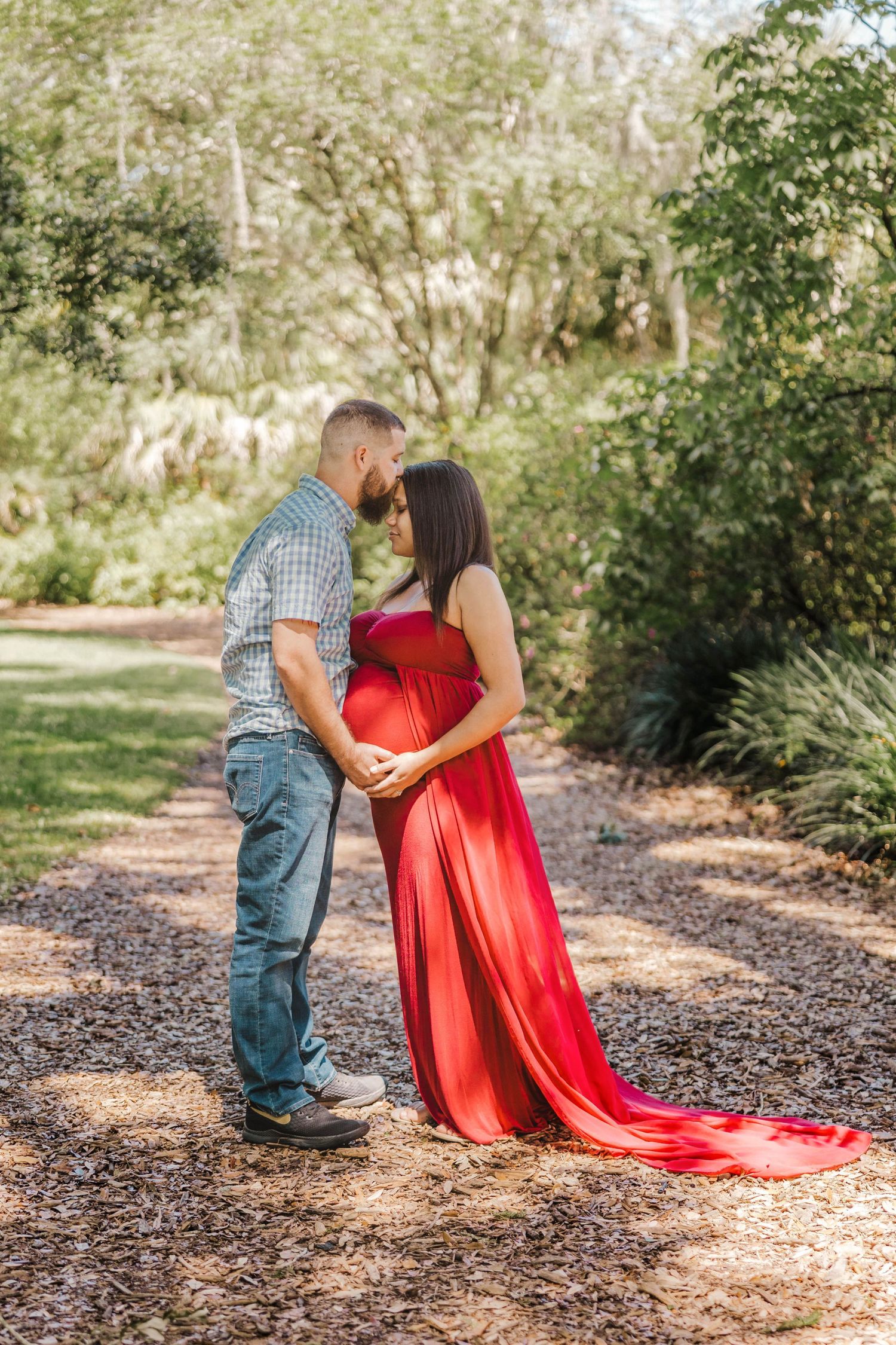 Couple holding hands and kissing over baby bump on a scenic garden path.