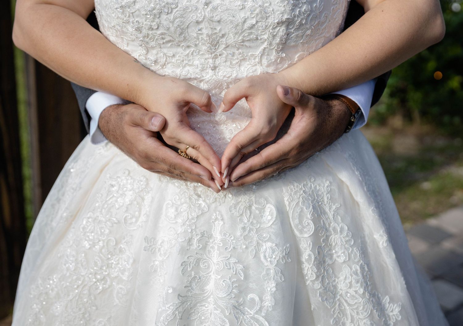 Bride and groom form a heart shape with their hands on the brides lace wedding gown.