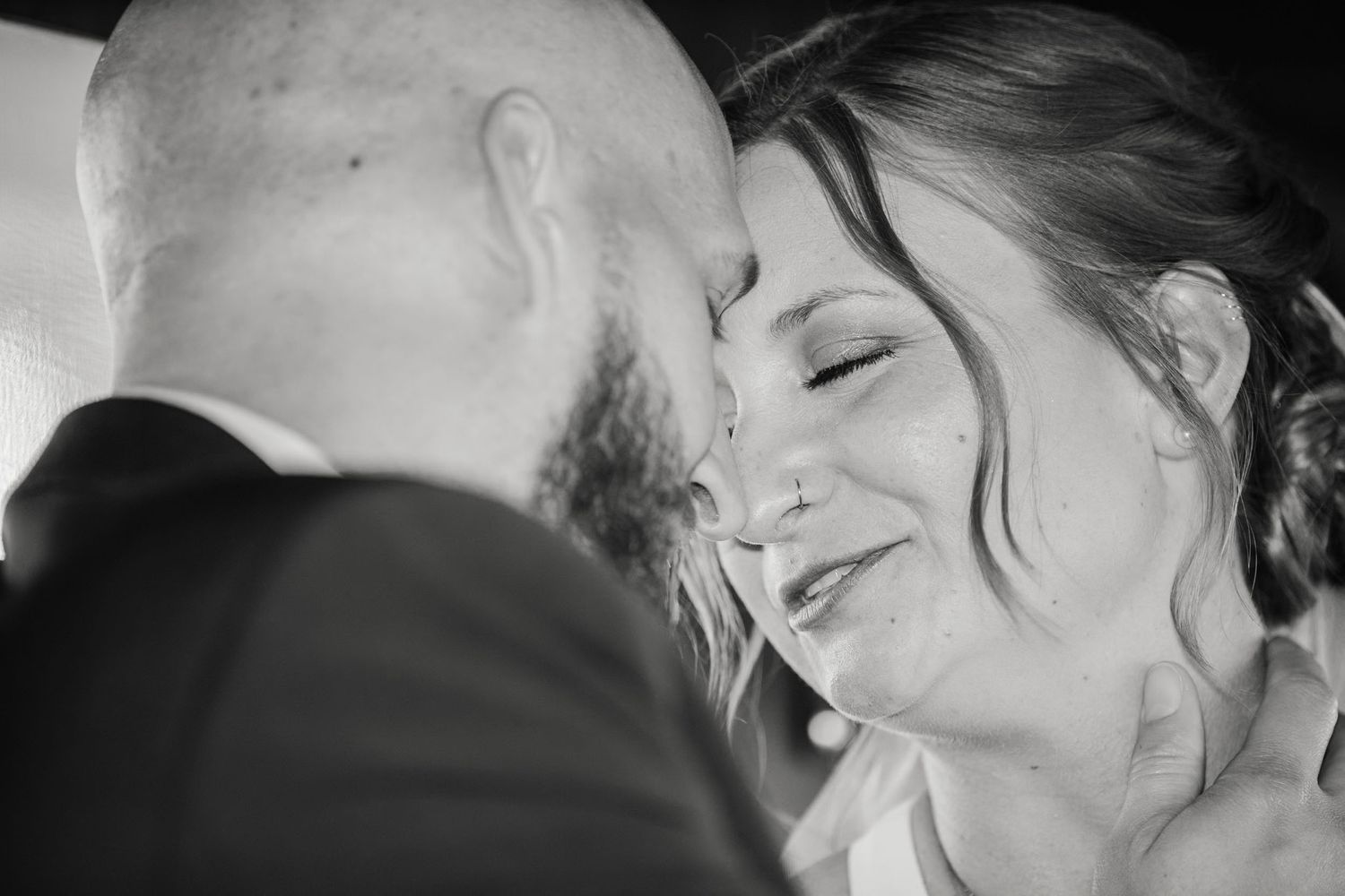 Black and white photo of bride smiling joyfully as groom tenderly kisses her forehead.