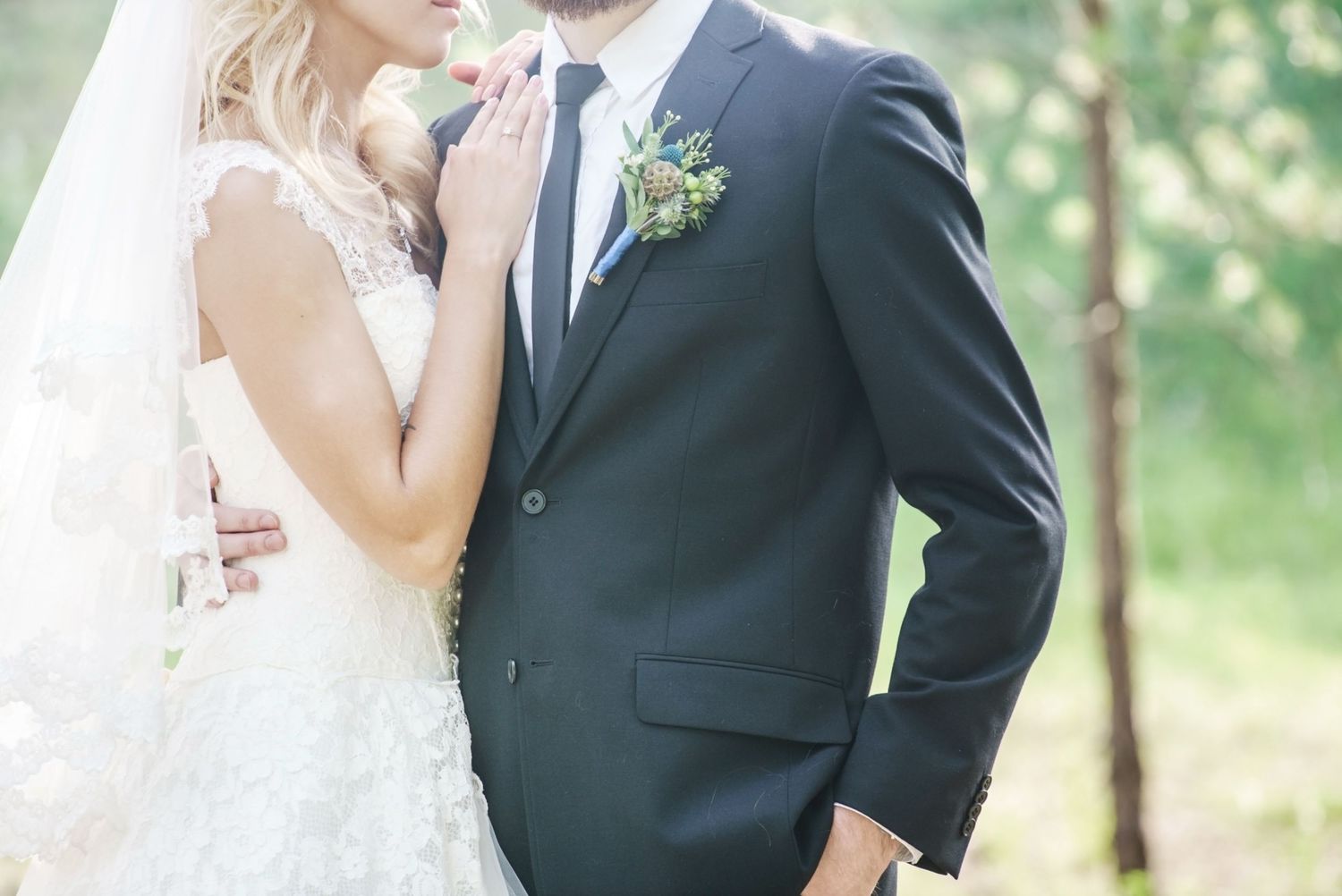 Bride and groom in wedding attire embracing outdoors, groom wearing navy suit with boutonniere.