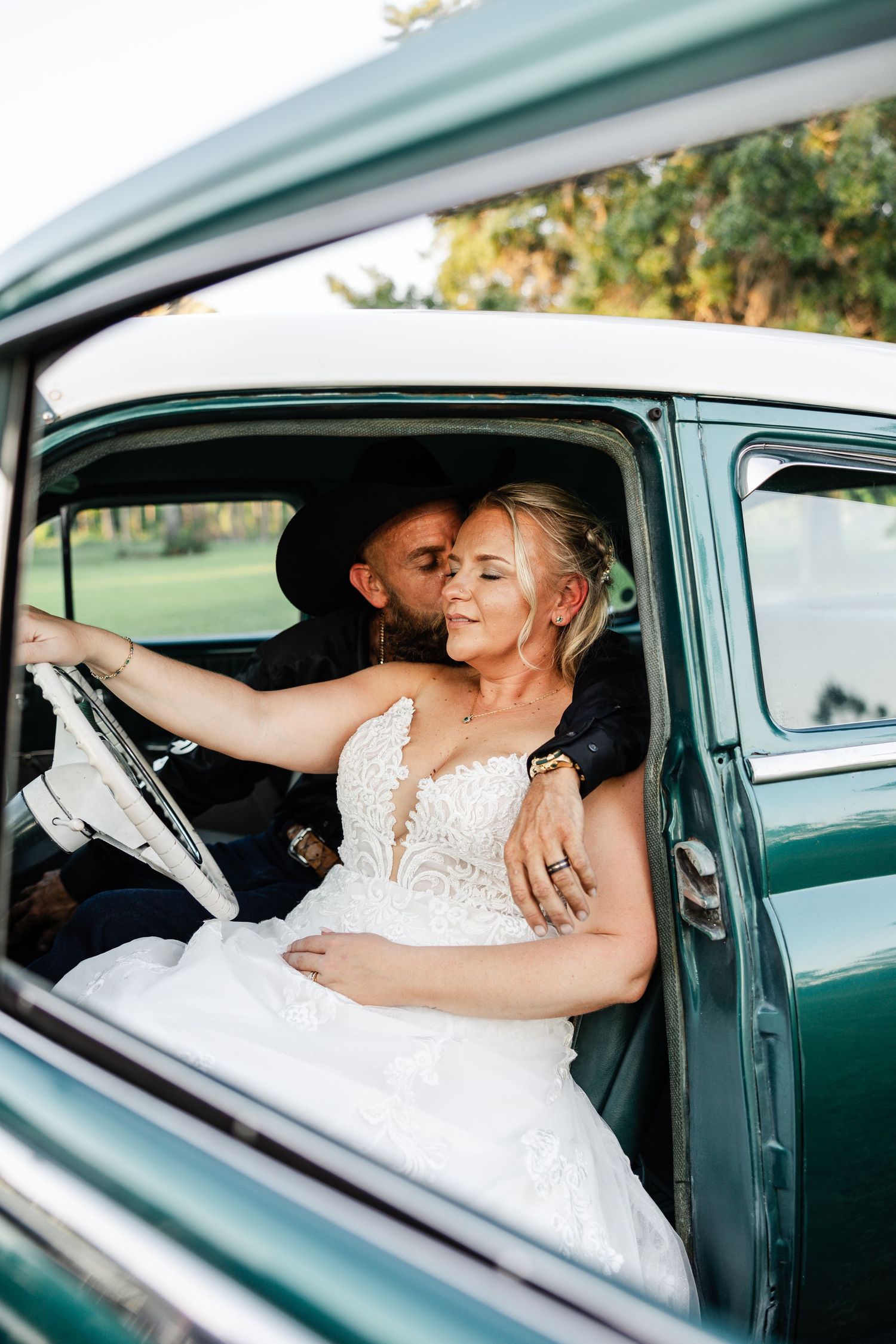 Bride and groom sharing a tender moment inside a vintage teal classic car.