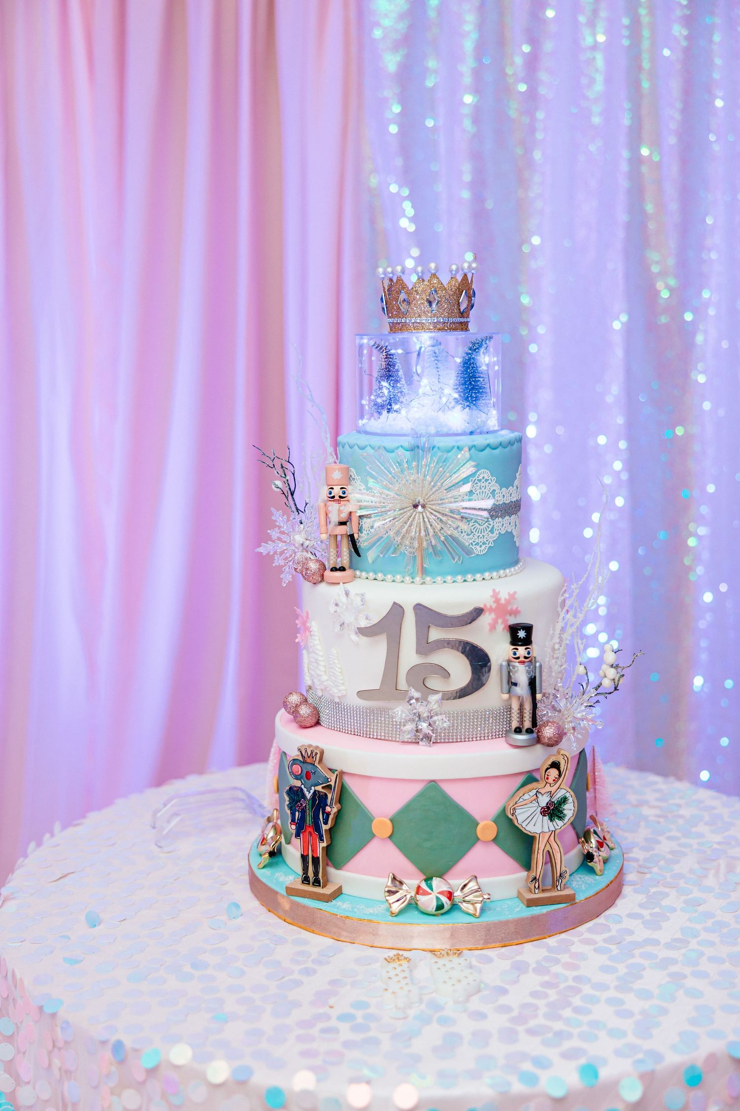Elegant four-tier quinceañera cake decorated with nutcrackers, ballerinas, and number 15 in pink and teal.