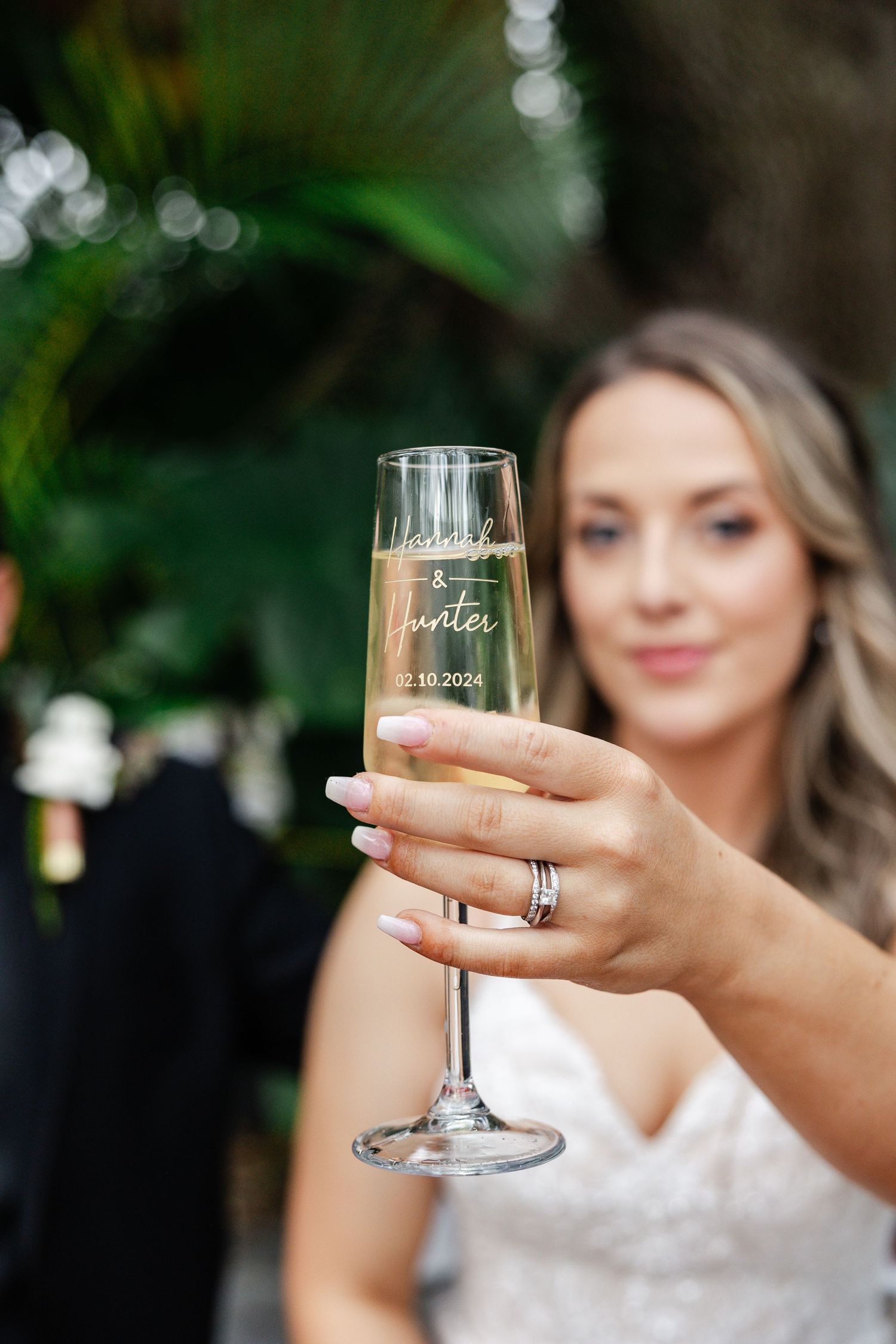 Bride holding personalized champagne flute engraved with wedding date 02.10.2024 at elegant celebration.