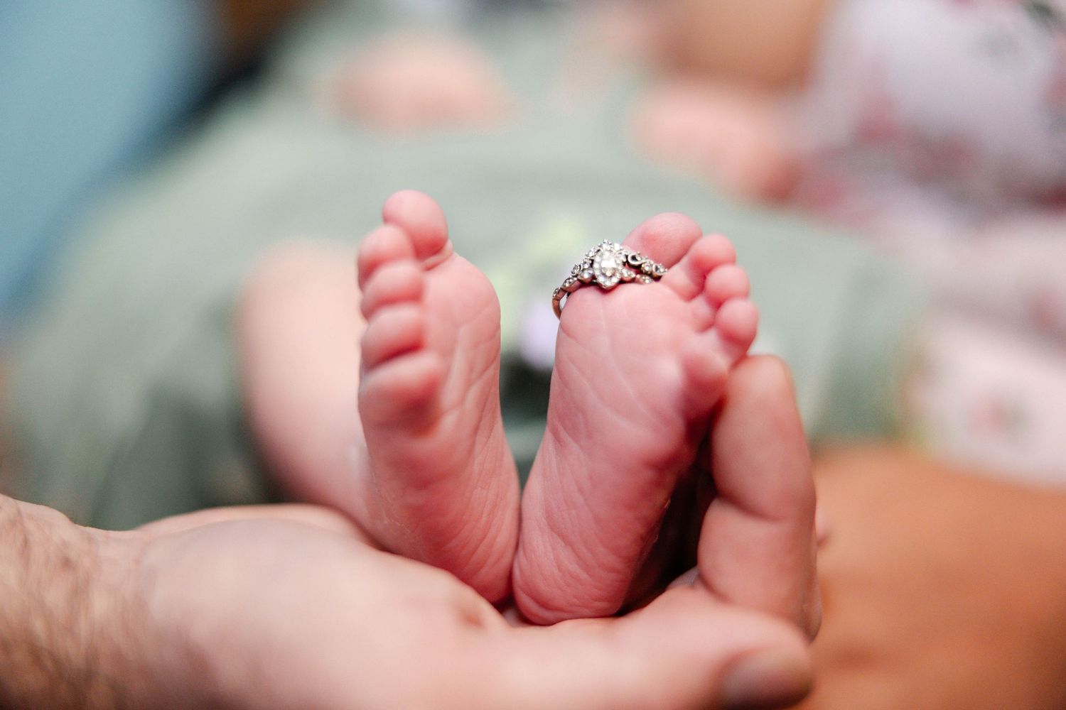 Close-up of tiny newborn baby feet resting in adult hands with a ring placed on toes.