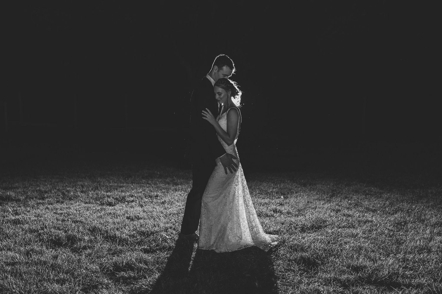 Dramatic black and white photo of bride and groom embracing in a dark field on their wedding night.