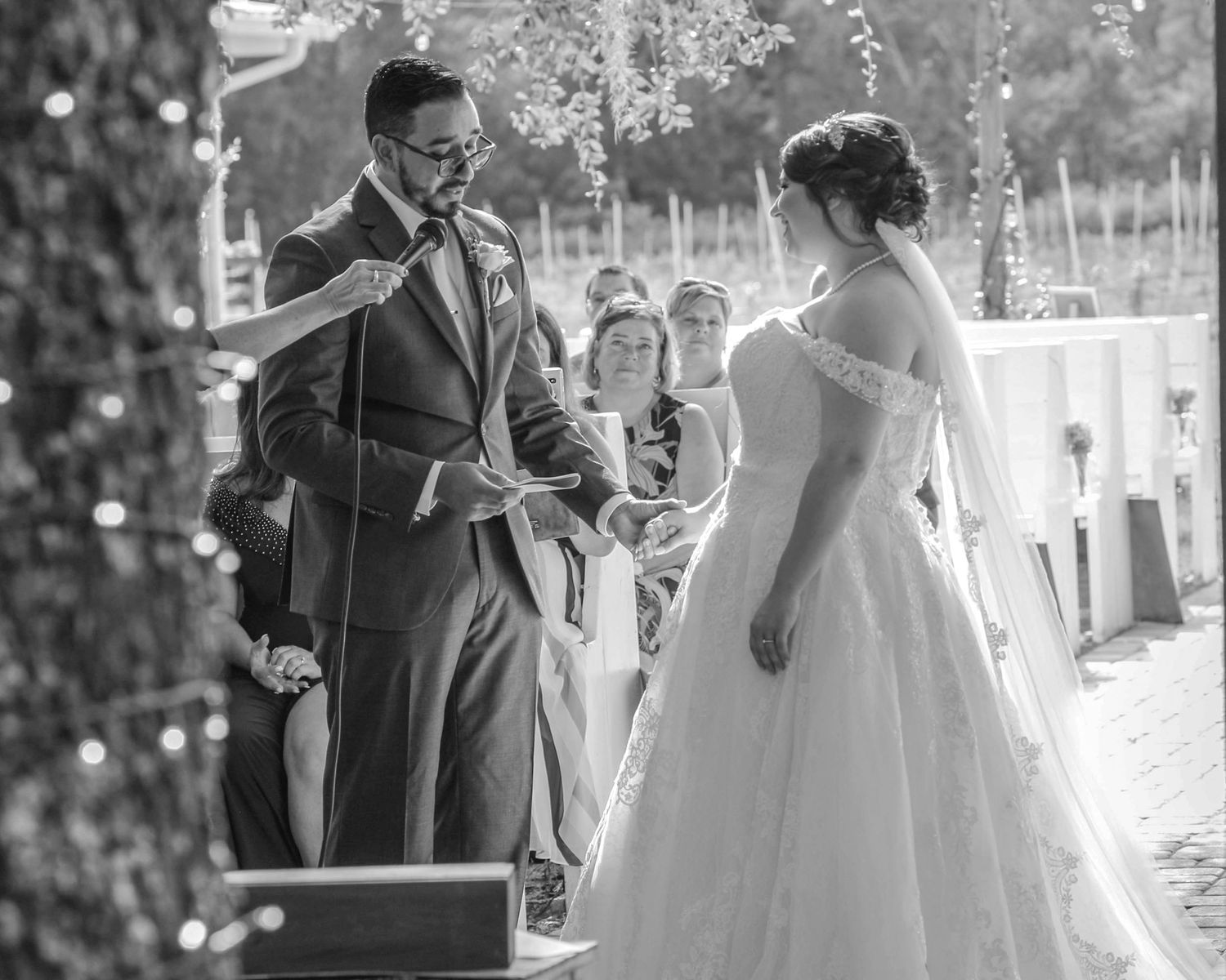 Black and white photo of groom reading vows to bride during outdoor wedding ceremony.