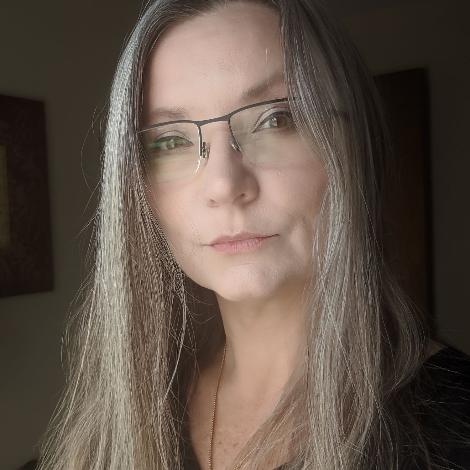 Close-up portrait of a woman with long gray hair wearing rectangular glasses against a dark background.