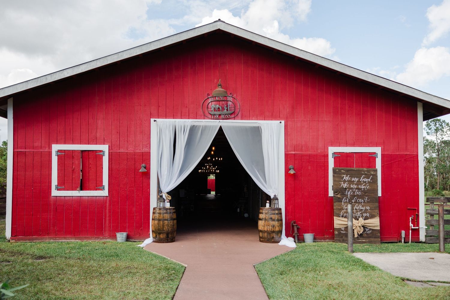 A charming red barn wedding venue with white draping and barrel decorations at the entrance.