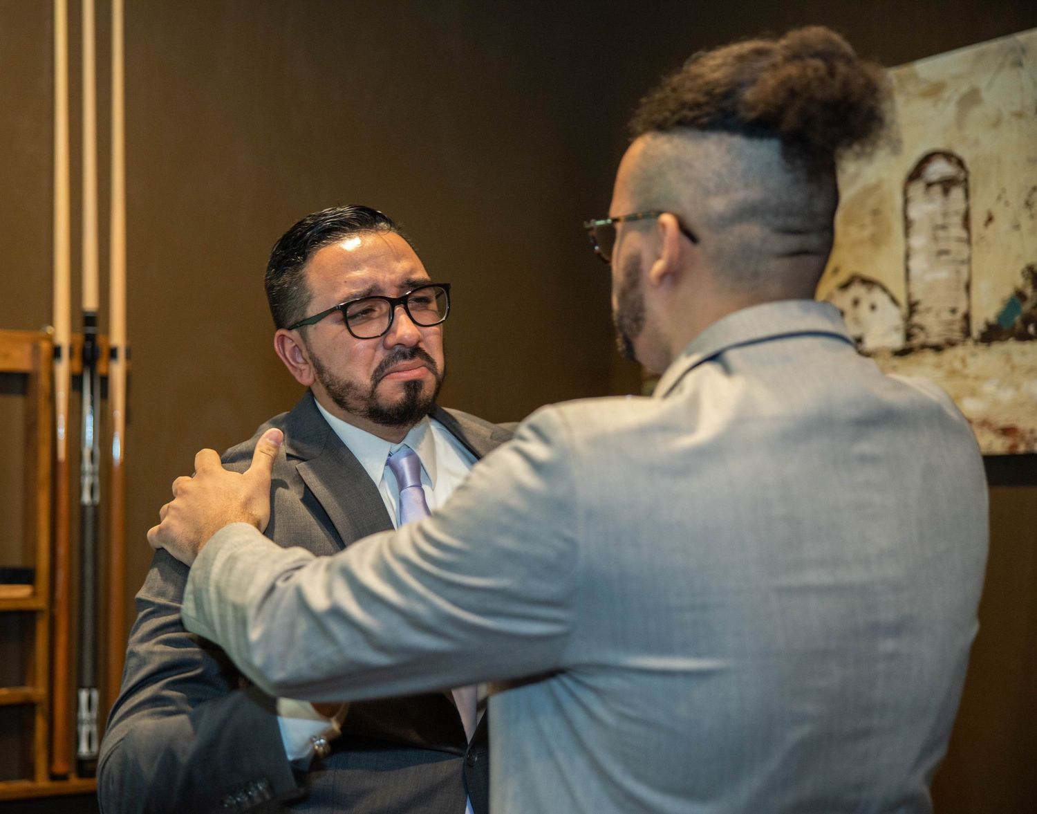 Two men in suits sharing an emotional moment with one placing a supportive hand on the others shoulder.