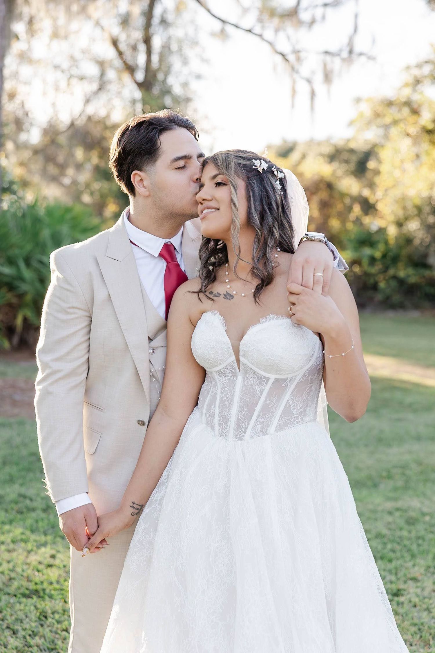 Groom in tan suit kisses bride in corset lace gown during romantic outdoor garden wedding.
