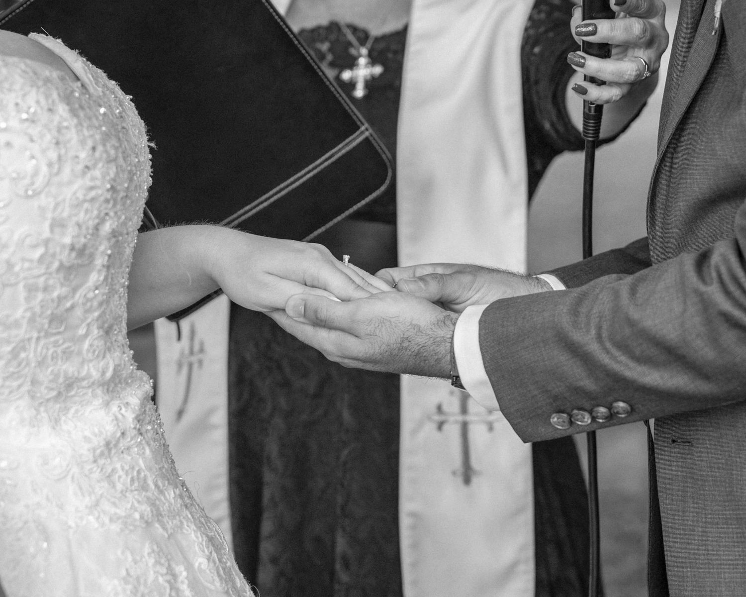 Close-up black and white photo of groom placing wedding ring on brides hand during ceremony.