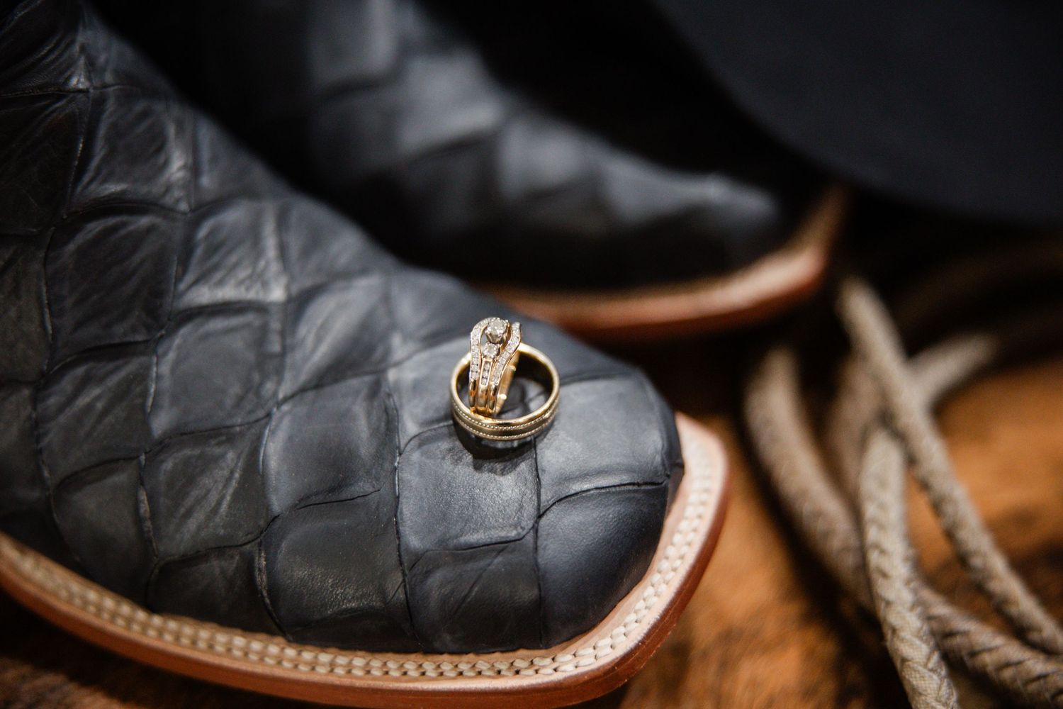 Gold wedding rings resting on black exotic leather cowboy boots with rope for rustic wedding.