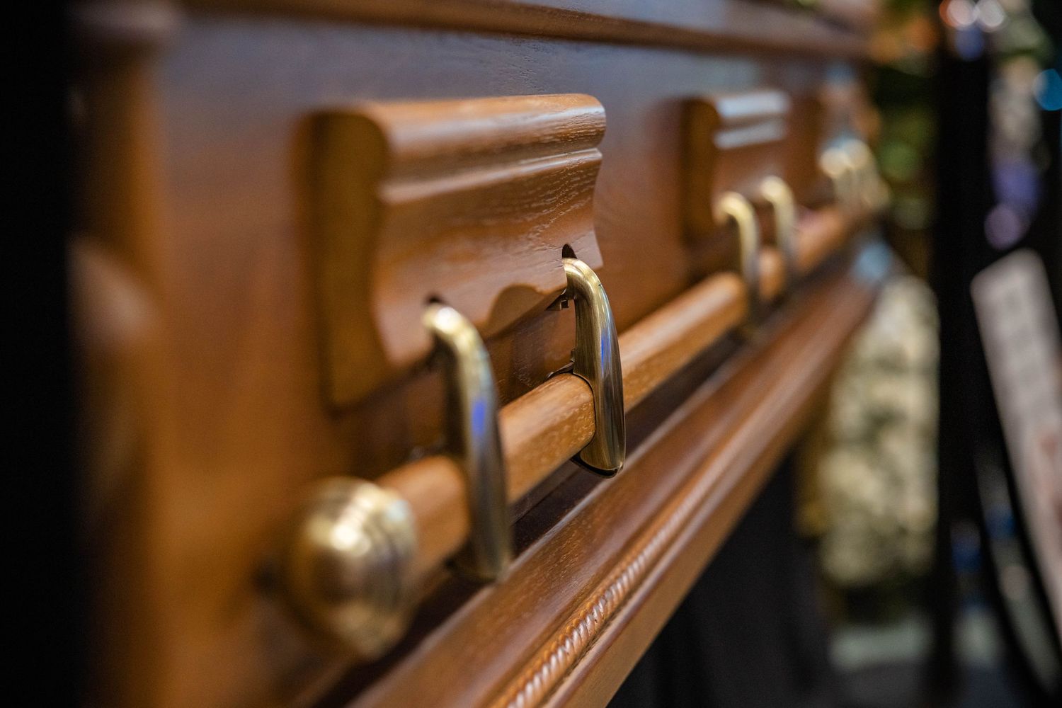 Close-up detail of polished wooden casket with brass handles at funeral service.