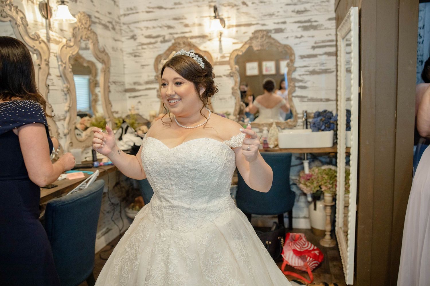 Bride in a white lace ball gown with tiara laughing joyfully during wedding preparations in a decorated room.