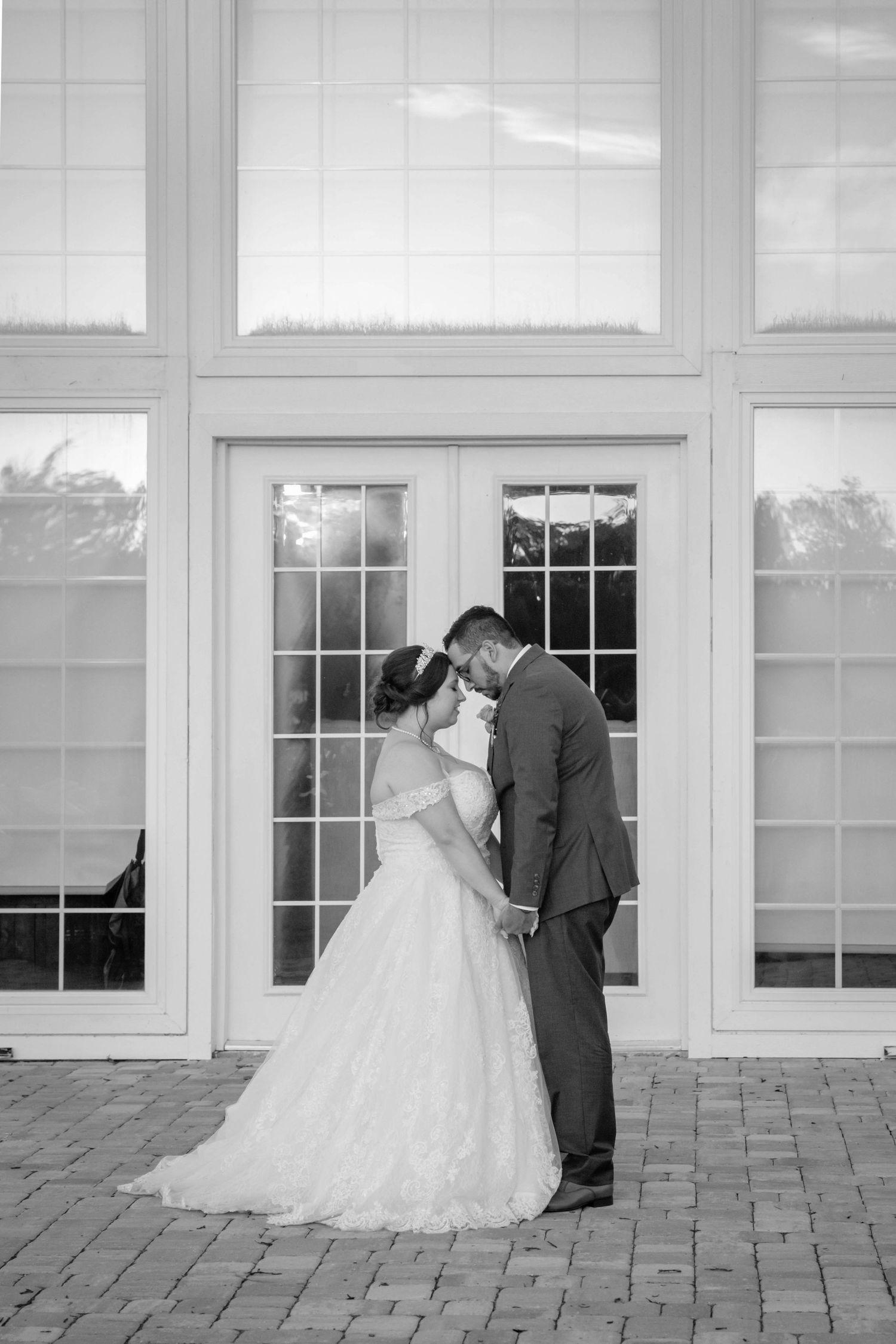 Bride and groom share a romantic moment in black and white photo outside elegant venue doors.