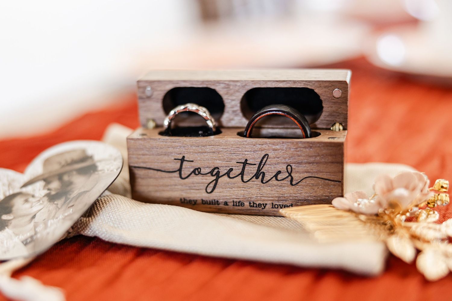 Wooden ring box engraved with together holding two wedding bands on red fabric.