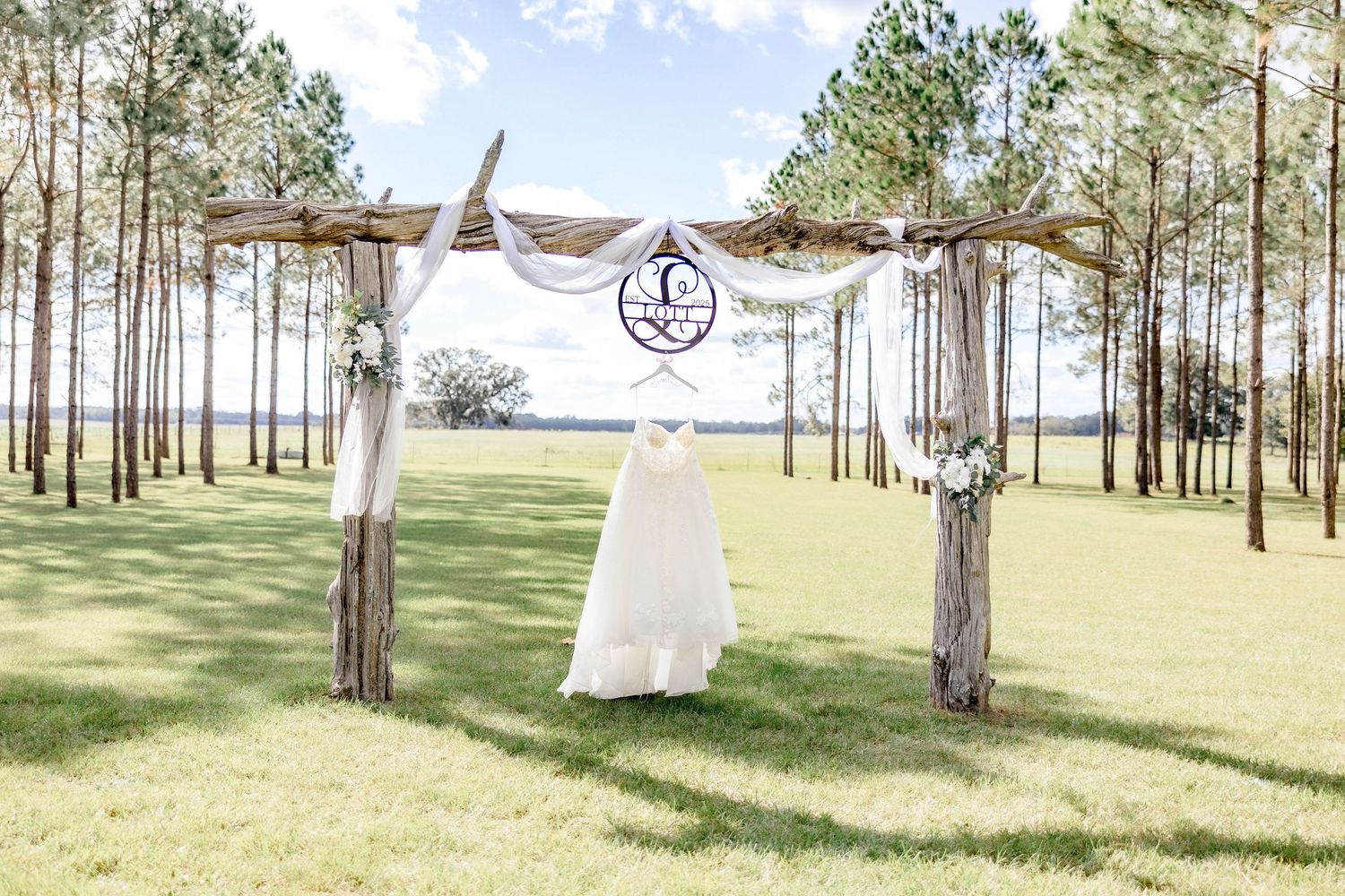 Wedding dress displayed on rustic wooden arbor with lake view and pine trees backdrop.