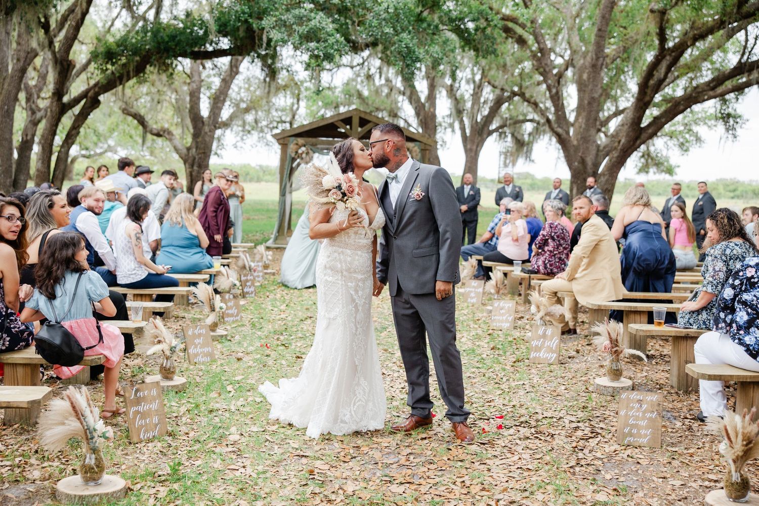 Bride and groom share first kiss at romantic outdoor wedding ceremony under oak trees.