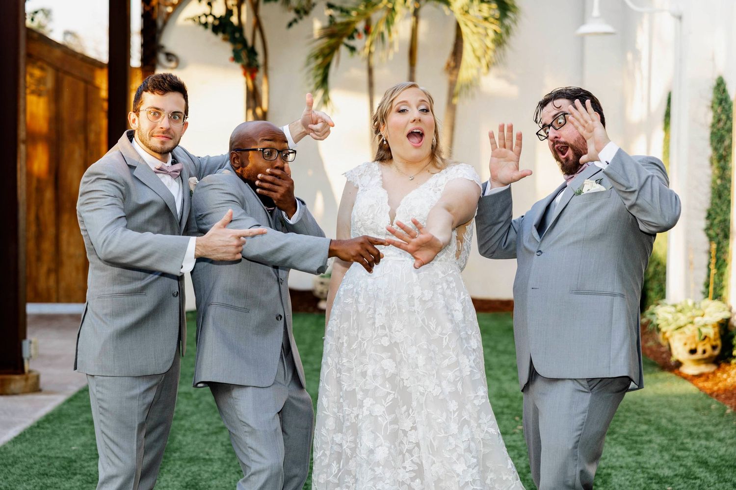 Bride and groomsmen in gray suits posing playfully outdoors at wedding venue.