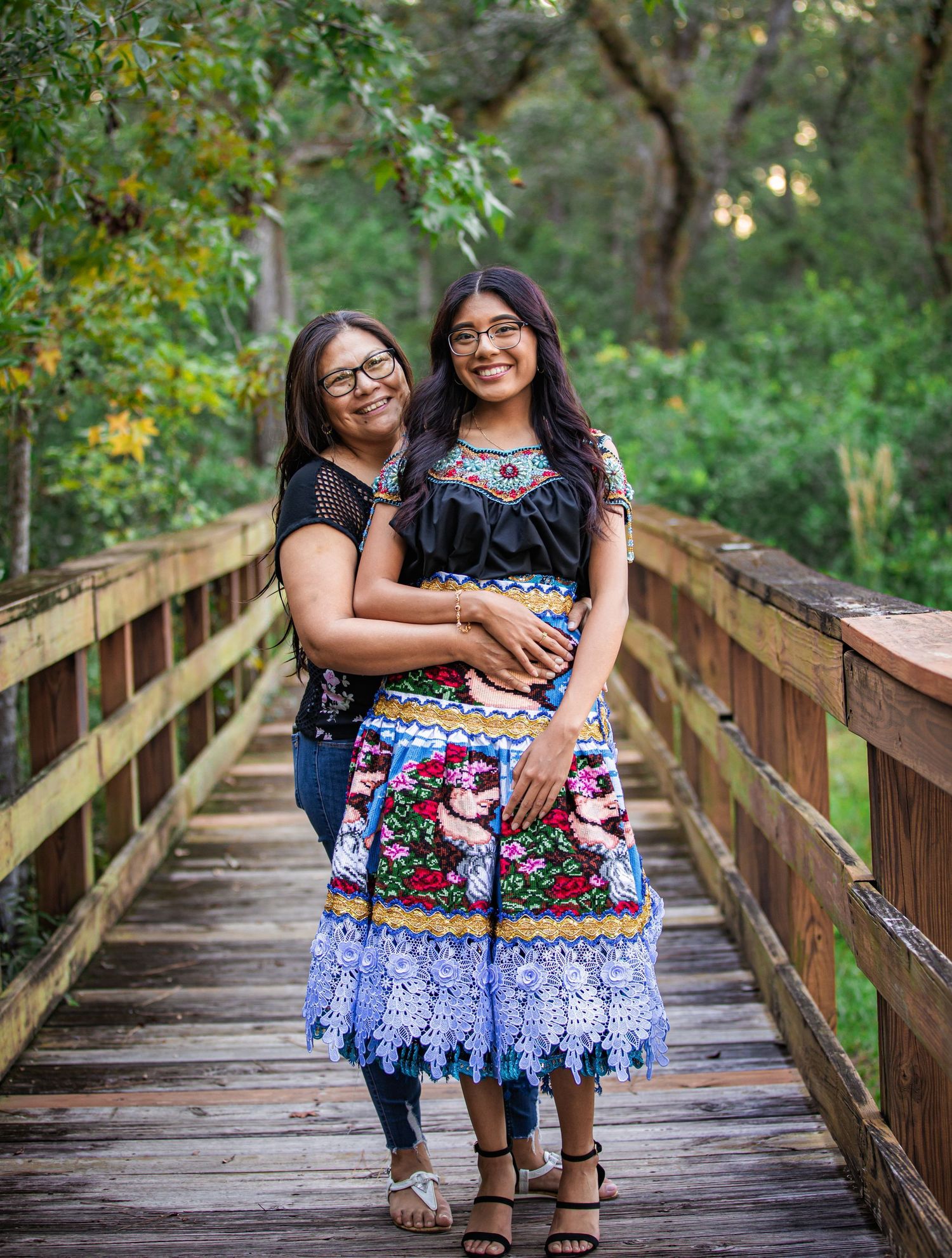 Mother and daughter smiling together on a wooden bridge wearing colorful outfits.