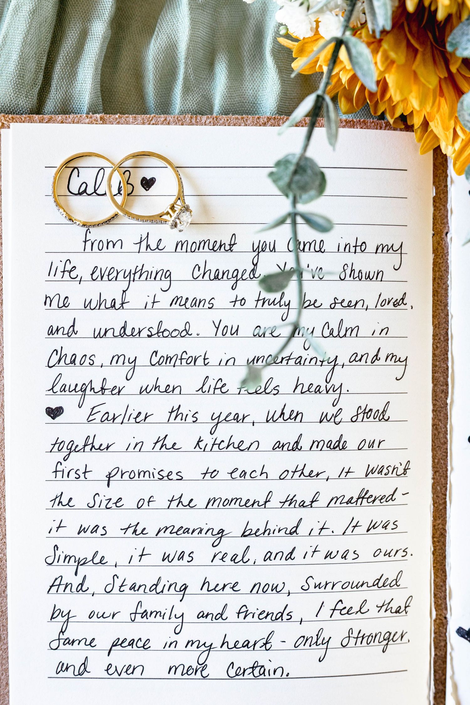Handwritten wedding vows on notebook paper with two gold rings and sunflower decoration.