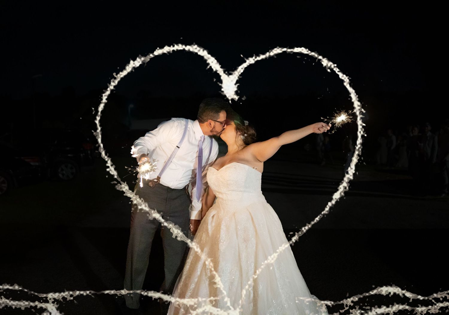 Bride and groom kiss inside a glowing sparkler heart shape created at night wedding celebration.