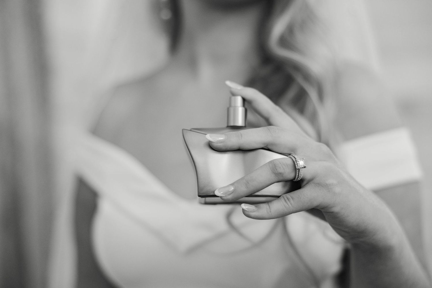 Black and white photo of bride in wedding dress holding perfume bottle before ceremony.