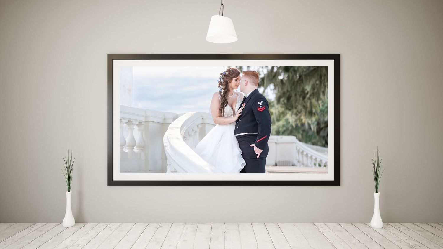 Framed wedding portrait of bride and groom embracing displayed on a wall above white vases.