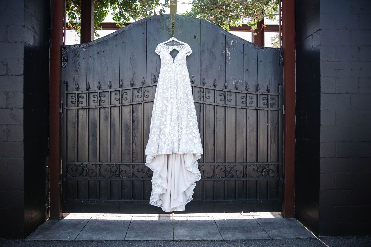 Elegant white lace wedding dress hanging on ornate black iron gates before the ceremony.
