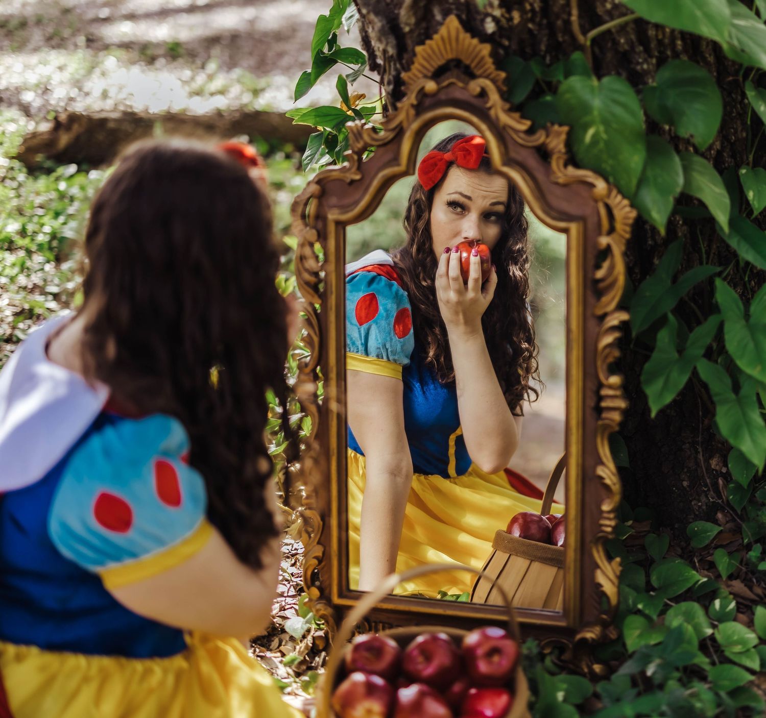 Woman dressed as Snow White in costume looking at her reflection in an ornate golden mirror outdoors.