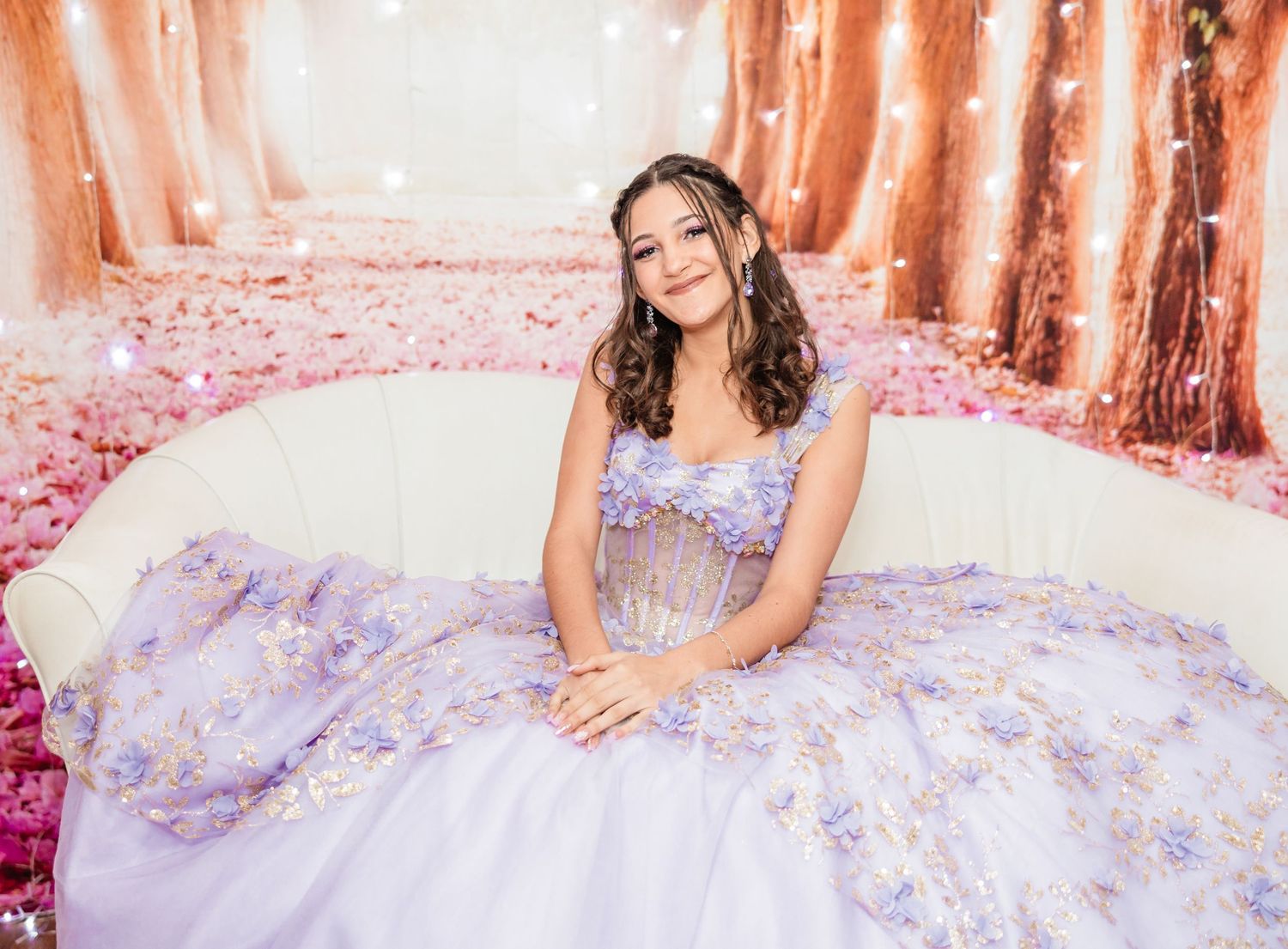 Teen girl in lavender floral quinceañera ball gown seated in white chair with bokeh lights.