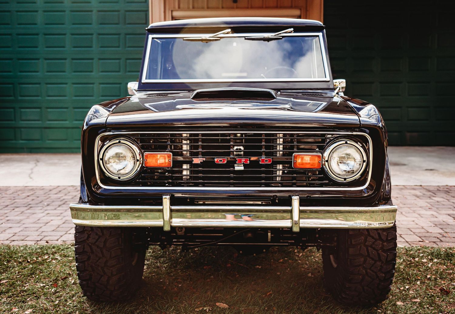 Restored black classic Ford Bronco 4x4 truck parked in front of green garage doors.