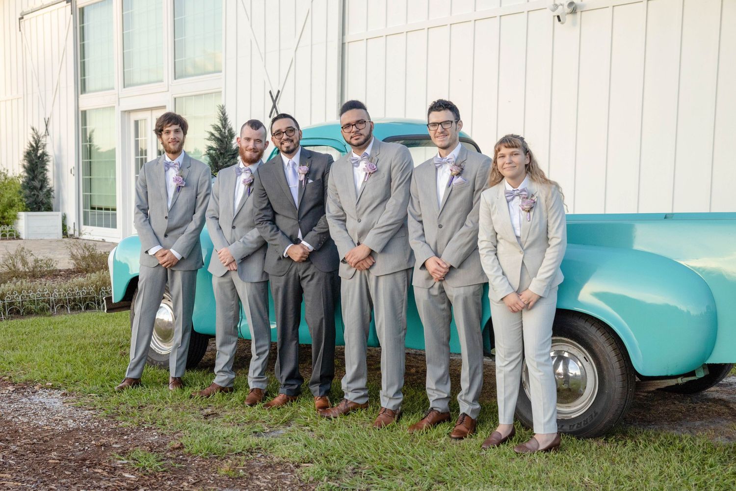 Groomsmen in gray suits pose with bride beside a vintage turquoise truck at wedding venue.