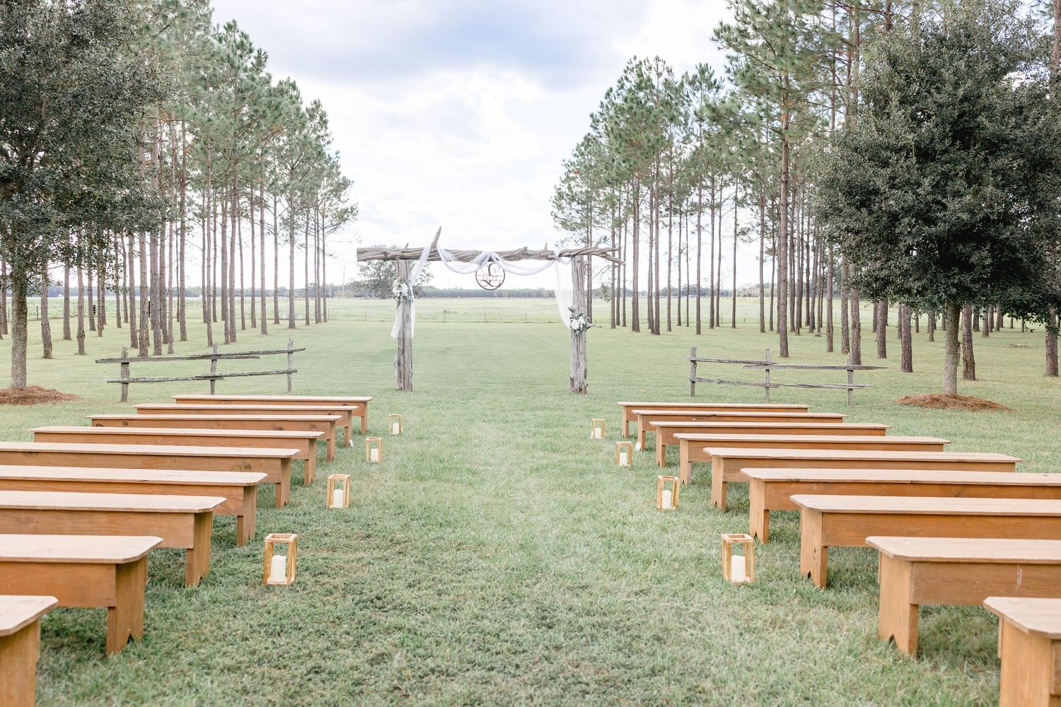 Outdoor wedding ceremony aisle lined with wooden benches leading to a rustic wooden arbor.