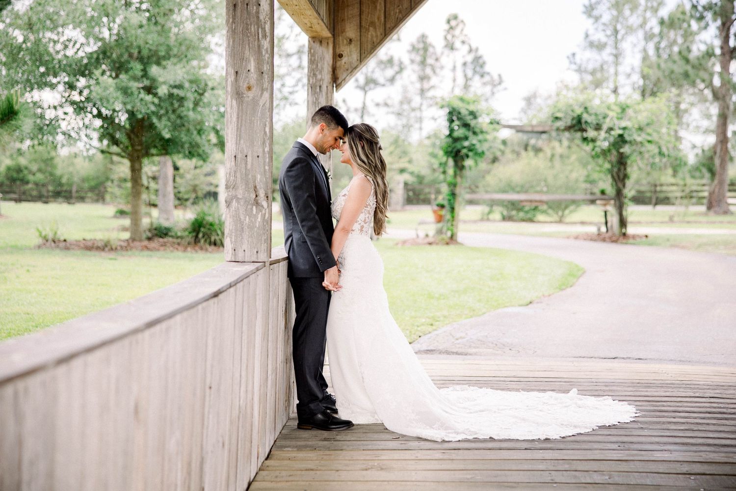 Bride and groom sharing an intimate moment on a wooden deck surrounded by lush green trees.